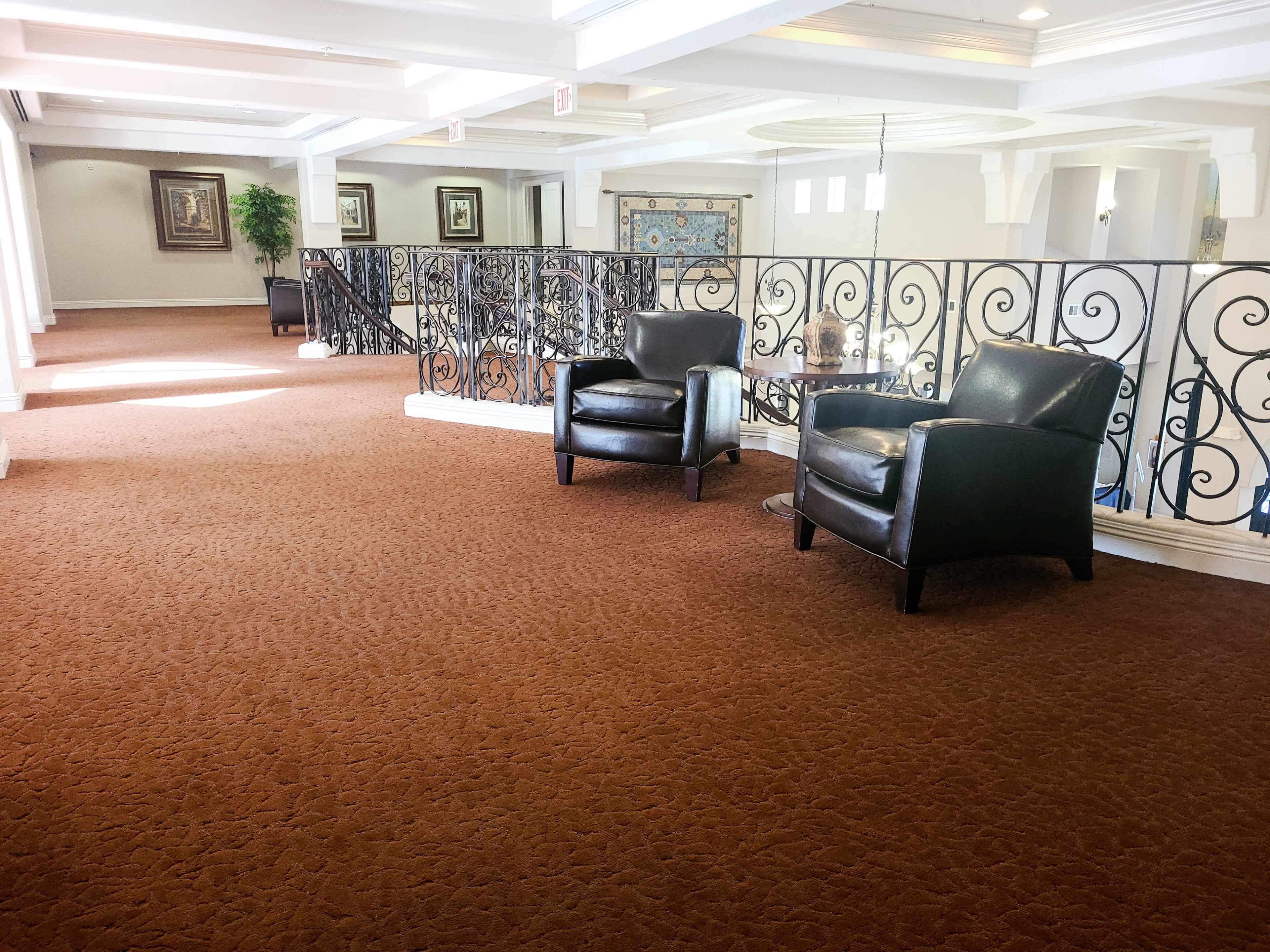 A corridor with brown carpet and two black leather armchairs near a decorative iron railing.