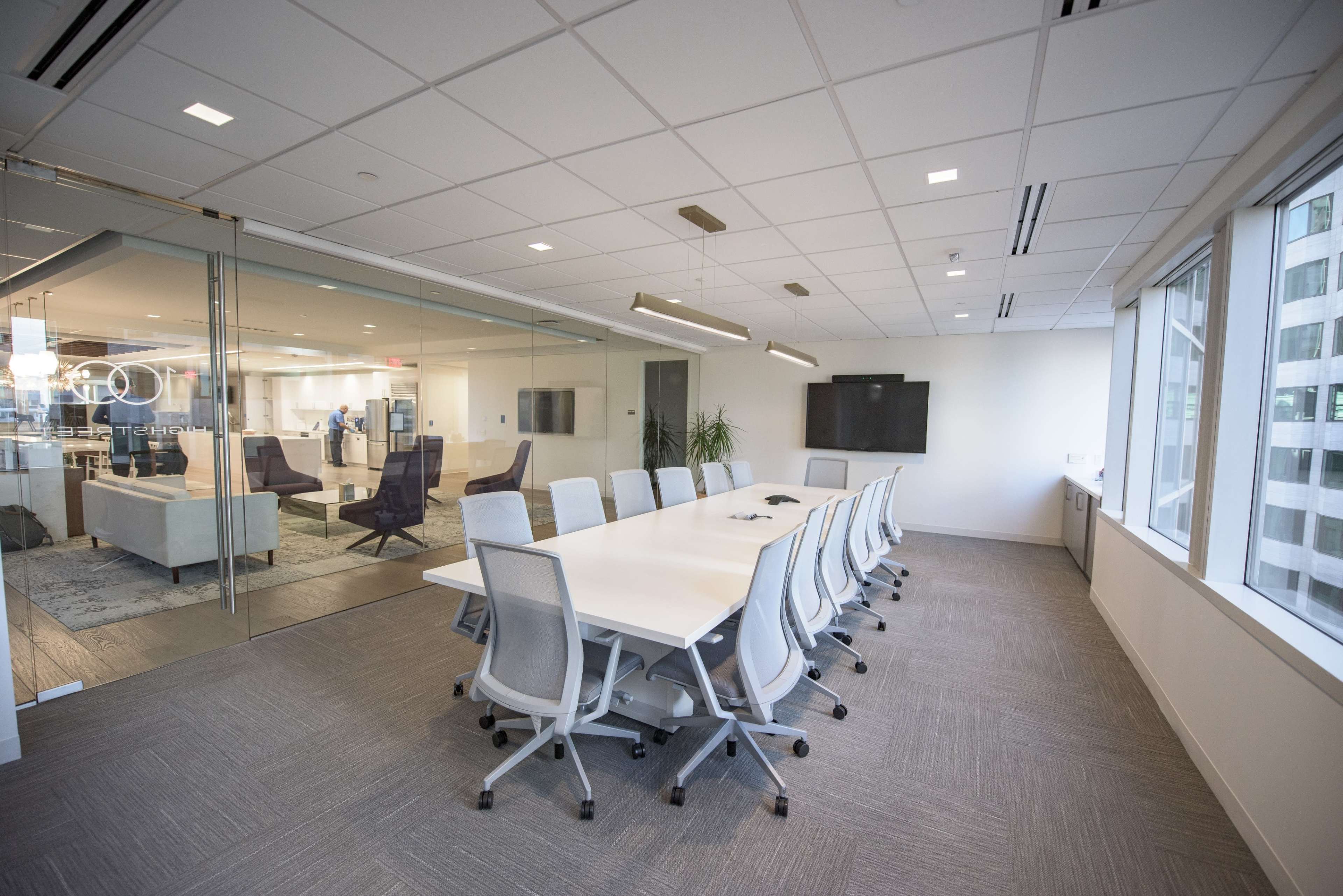 A modern conference room with a long white table surrounded by ergonomic chairs, featuring large windows and glass walls.