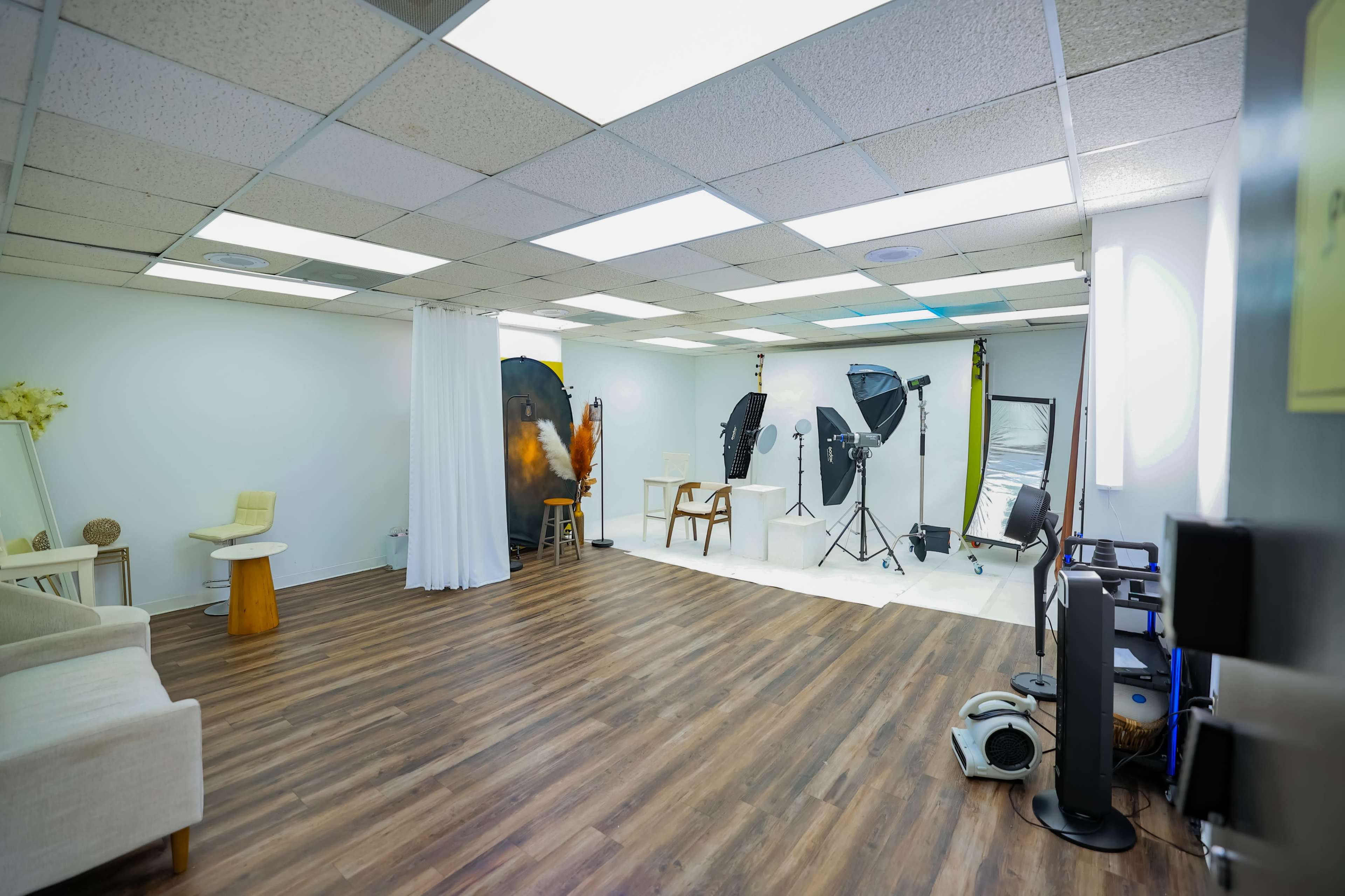 The image shows a spacious photography studio equipped with lighting equipment, a backdrop, and a seating area.