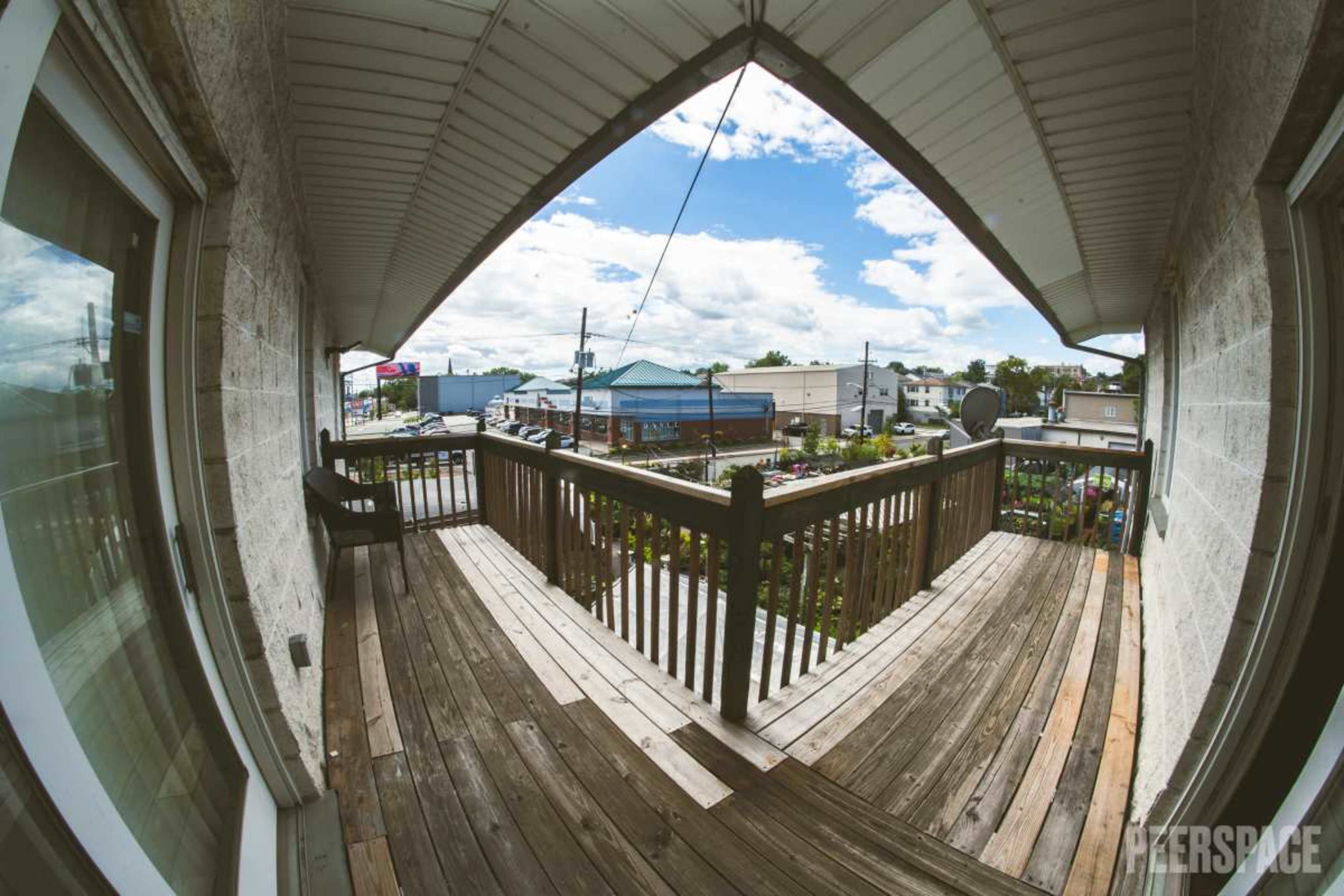 The image shows a fish-eye view from a balcony overlooking a parking lot and several buildings under a partly cloudy sky.
