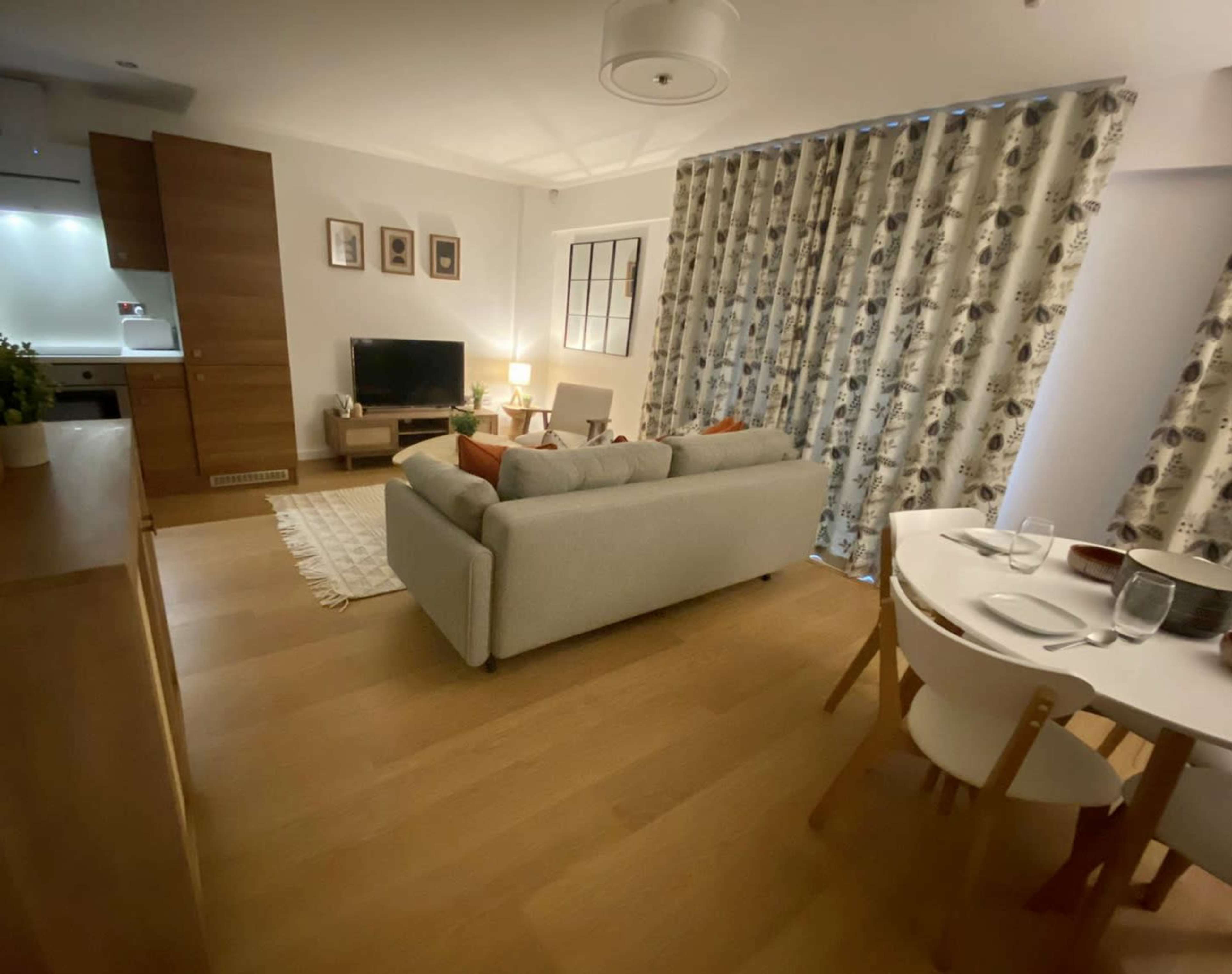 A modern living space with a sofa, coffee table, TV, and a dining area featuring a round table and chairs.