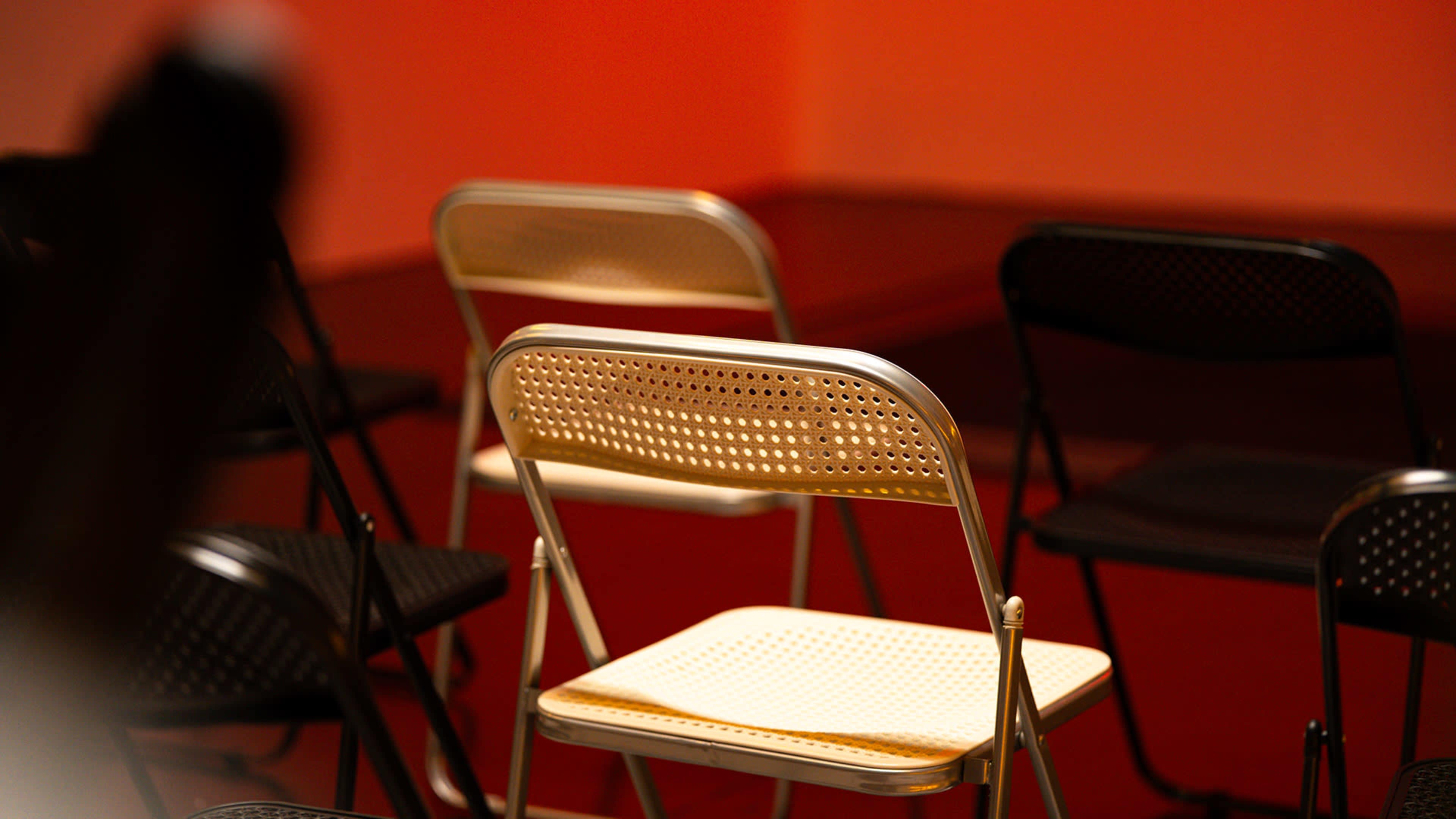 A group of folding chairs, both black and white, are arranged in a red room with a softly lit background.