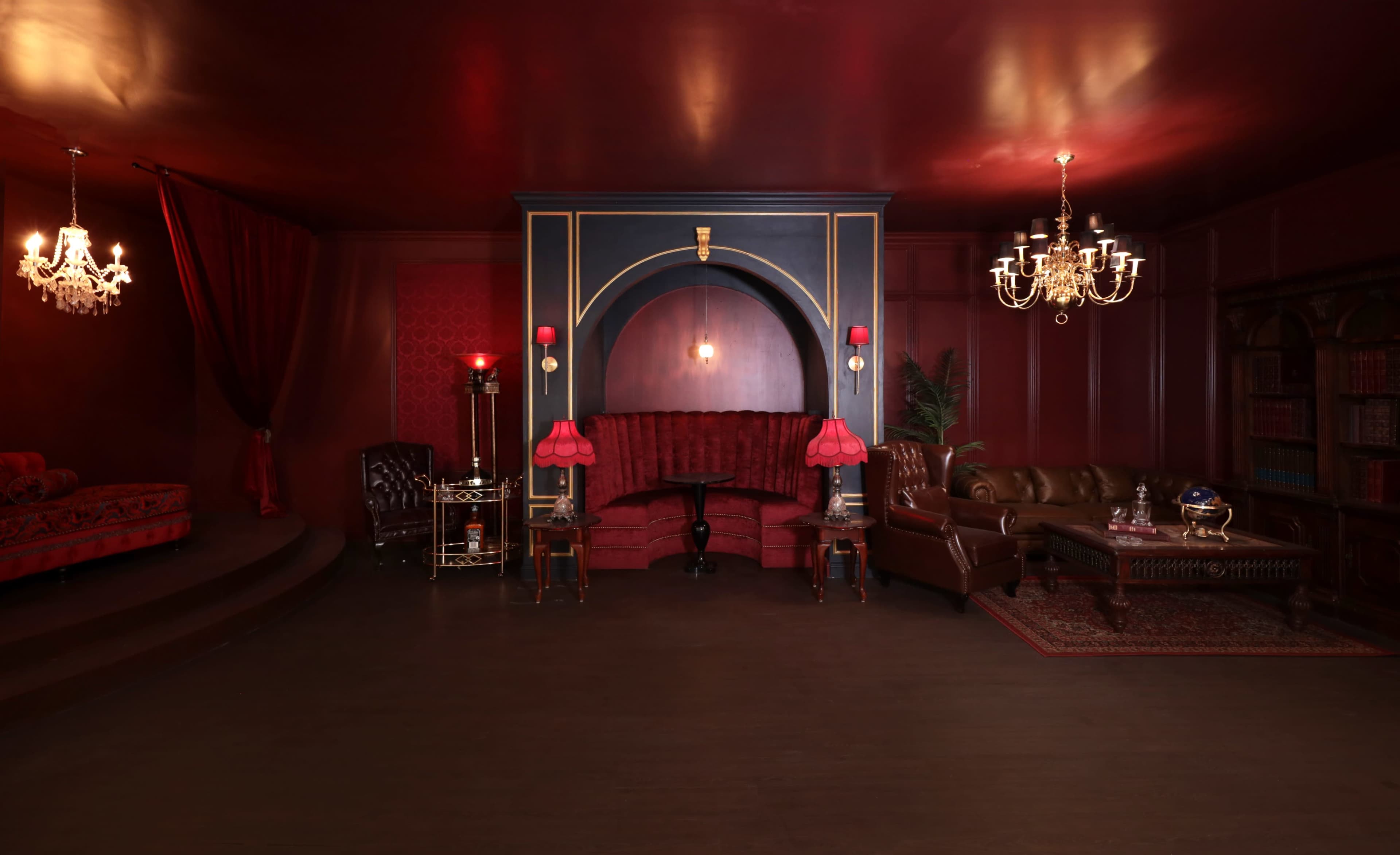 The room features deep red walls, ornate lighting fixtures, and elegant furniture arranged in a cozy setting.
