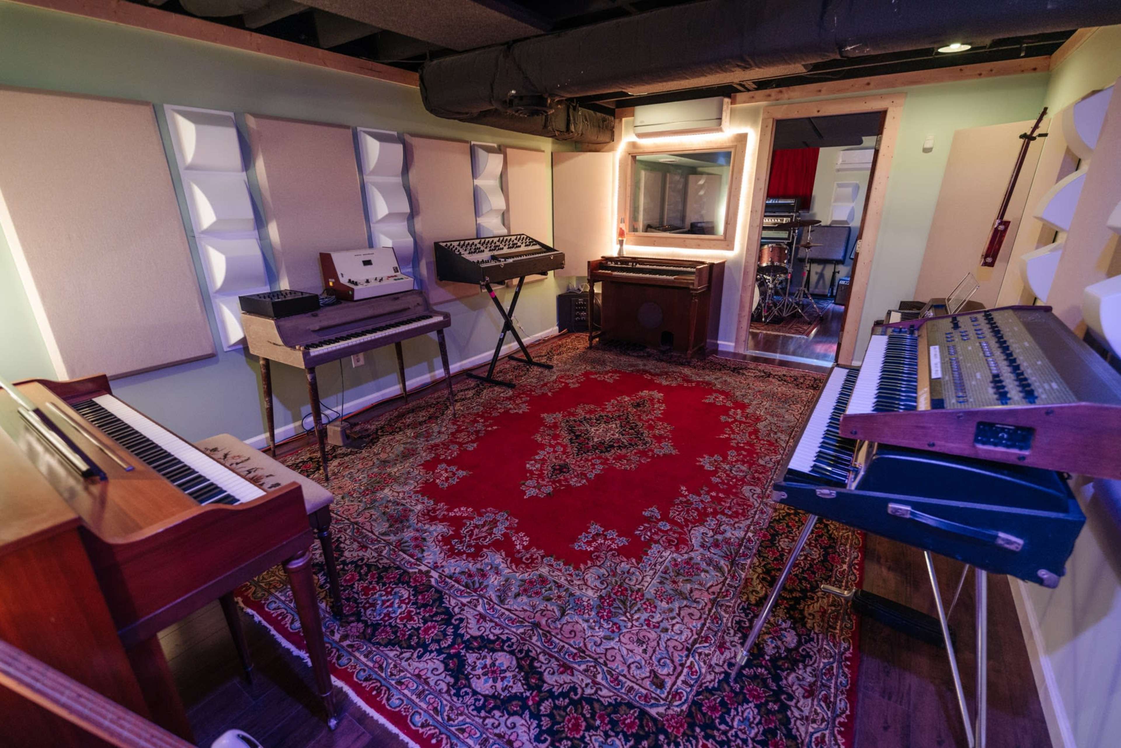 A soundproof music studio featuring various keyboards and synthesizers arranged around a patterned rug.