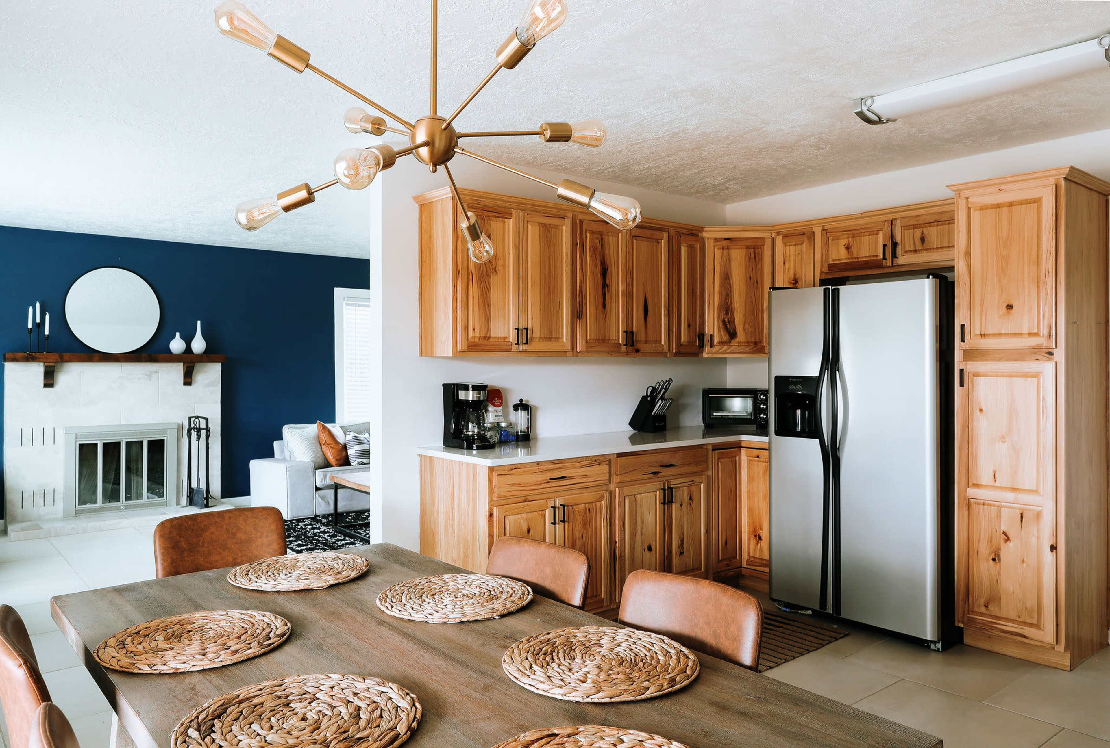 A modern kitchen features wood cabinetry, stainless steel appliances, a dining table set with woven placemats, and a blue accent wall.