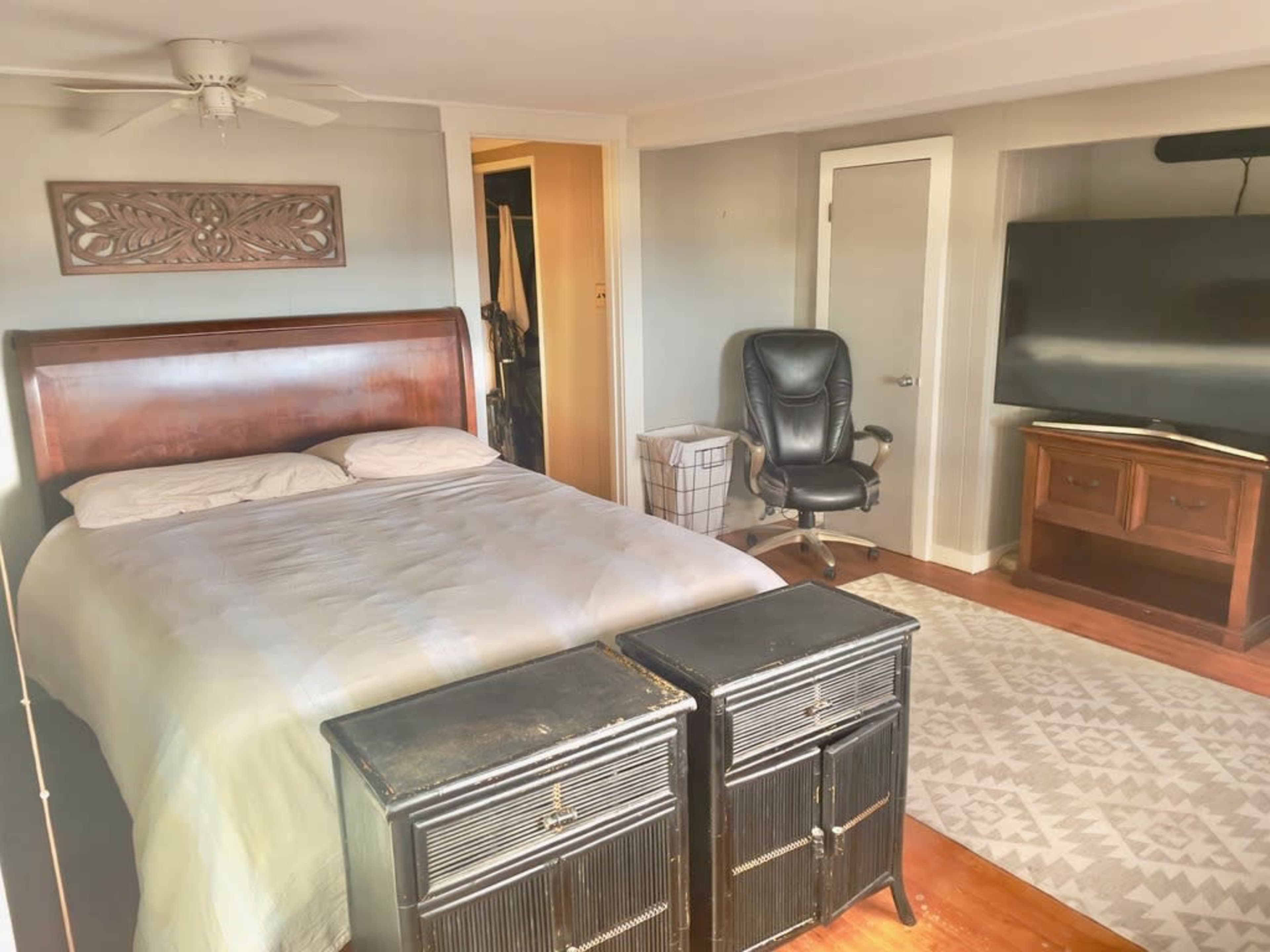 A bedroom with a bed, two black nightstands, a chair, a television, and a closet.