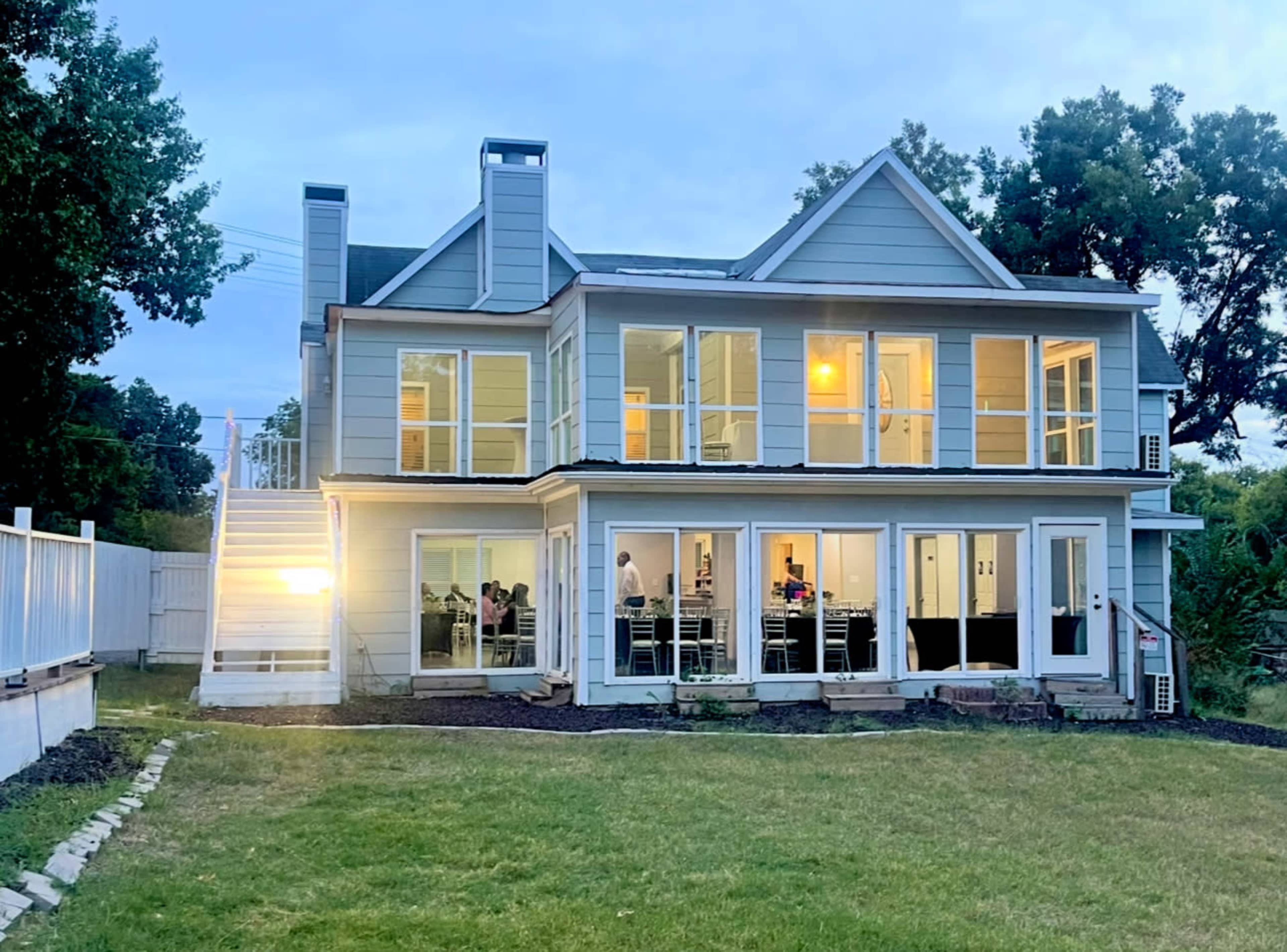 A large two-story house features multiple windows and a grassy backyard, illuminated in the evening light.