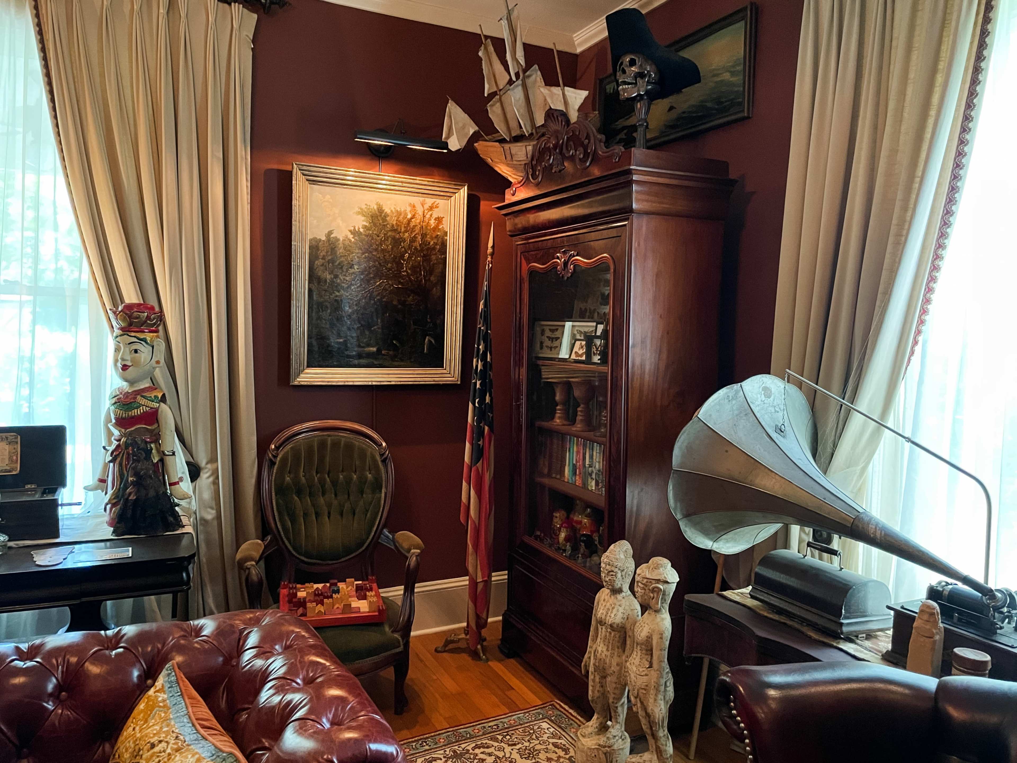 The room features a vintage sofa, a large wooden cabinet with books, a classic gramophone, an American flag, a painting of a landscape, and decorative statues.