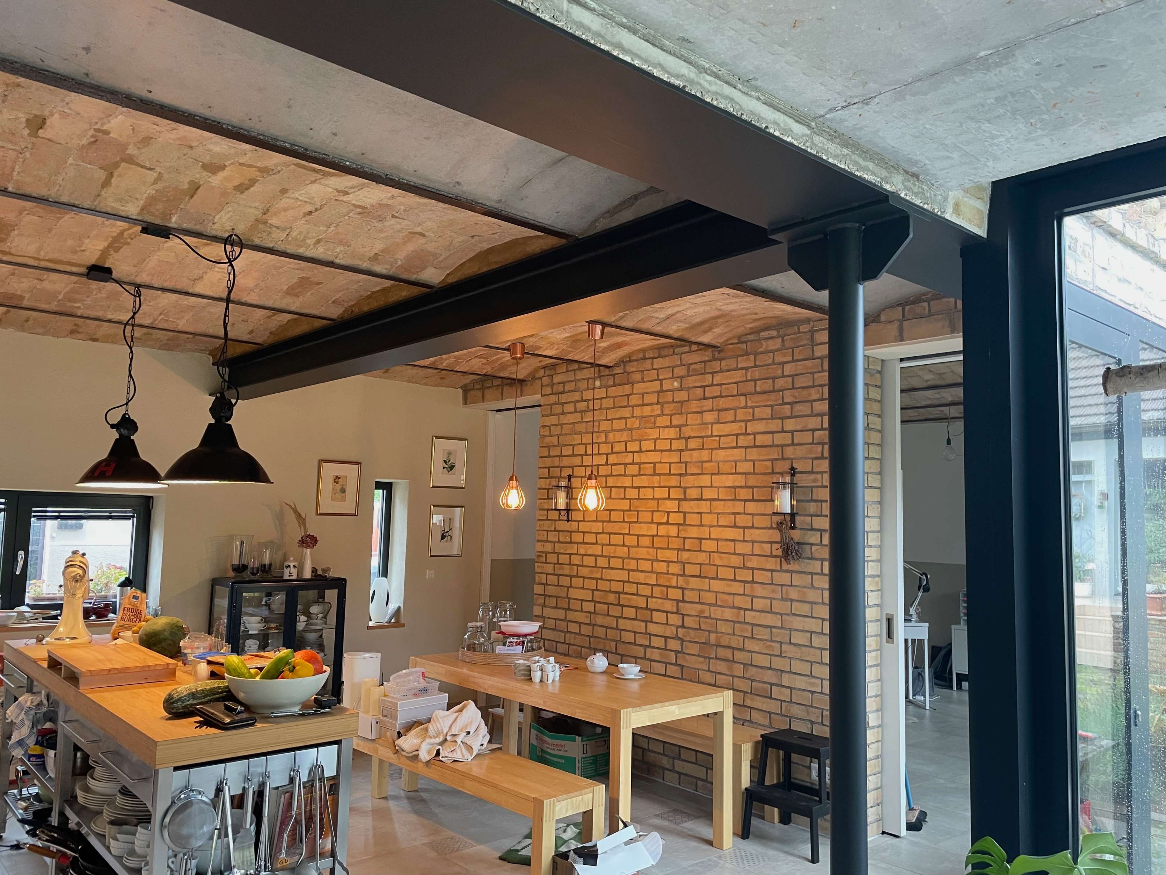 The image shows a modern kitchen with exposed brick walls, wooden tables, and industrial-style lighting.