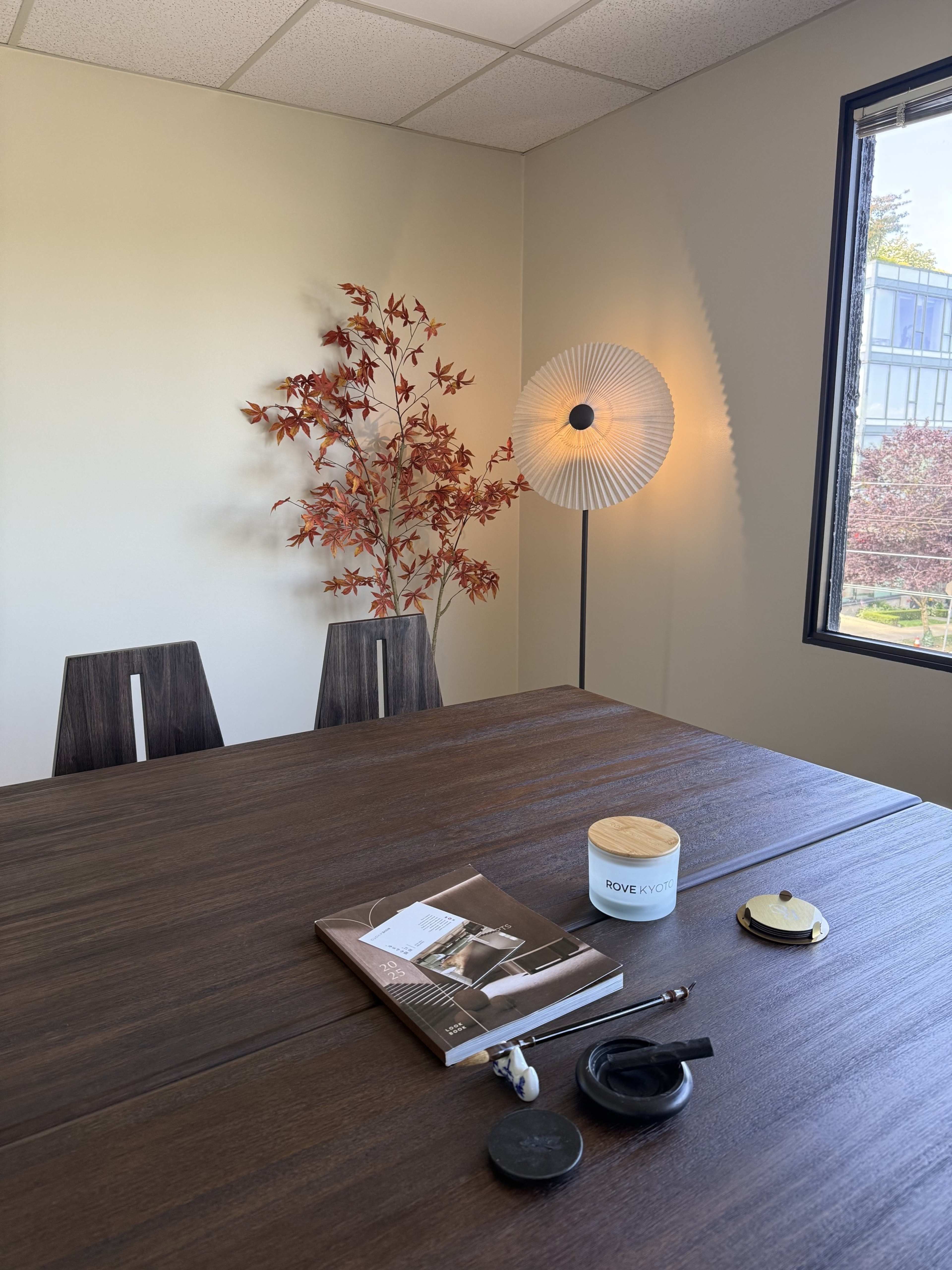 The image shows a modern conference room with a wooden table, two chairs, a decorative plant, a lamp, and several objects arranged on the table.