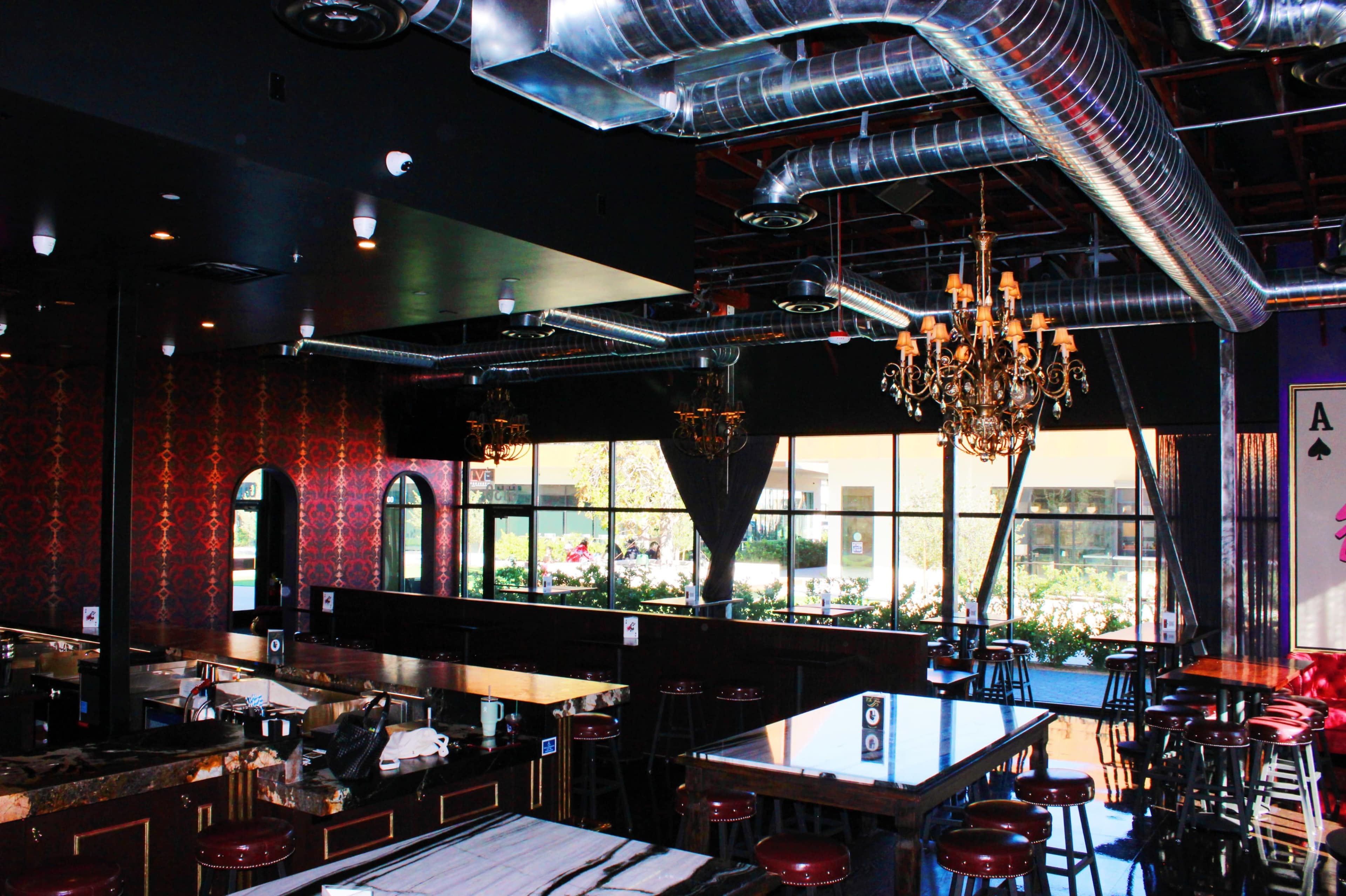 The image shows the interior of a restaurant featuring dark decor, chandeliers, and large windows overlooking greenery.