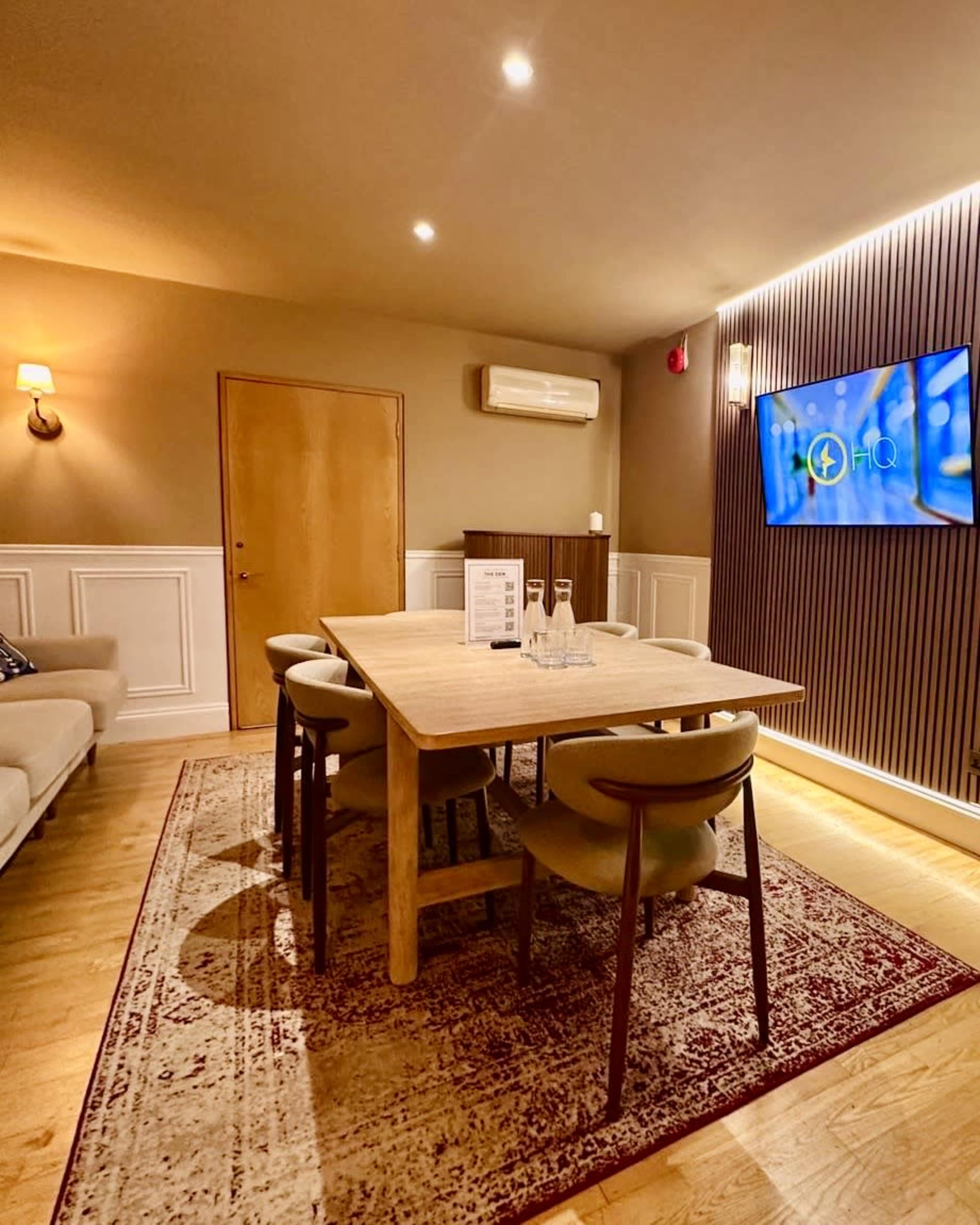 The image shows a modern meeting room with a wooden table and chairs, a television on the wall, and ambient lighting.