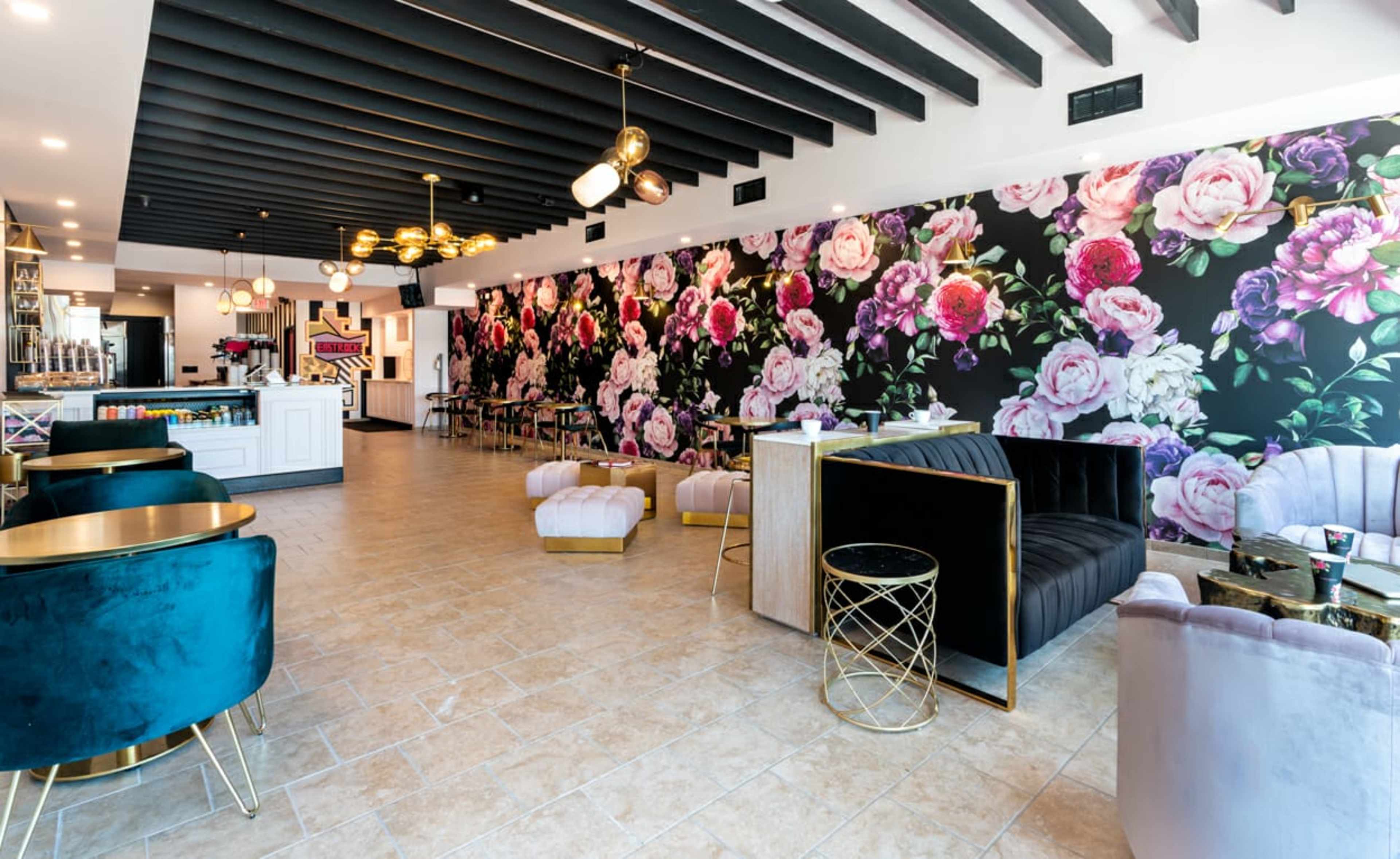 A modern café interior with a floral wallpaper, elegant seating arrangements, and gold accents.