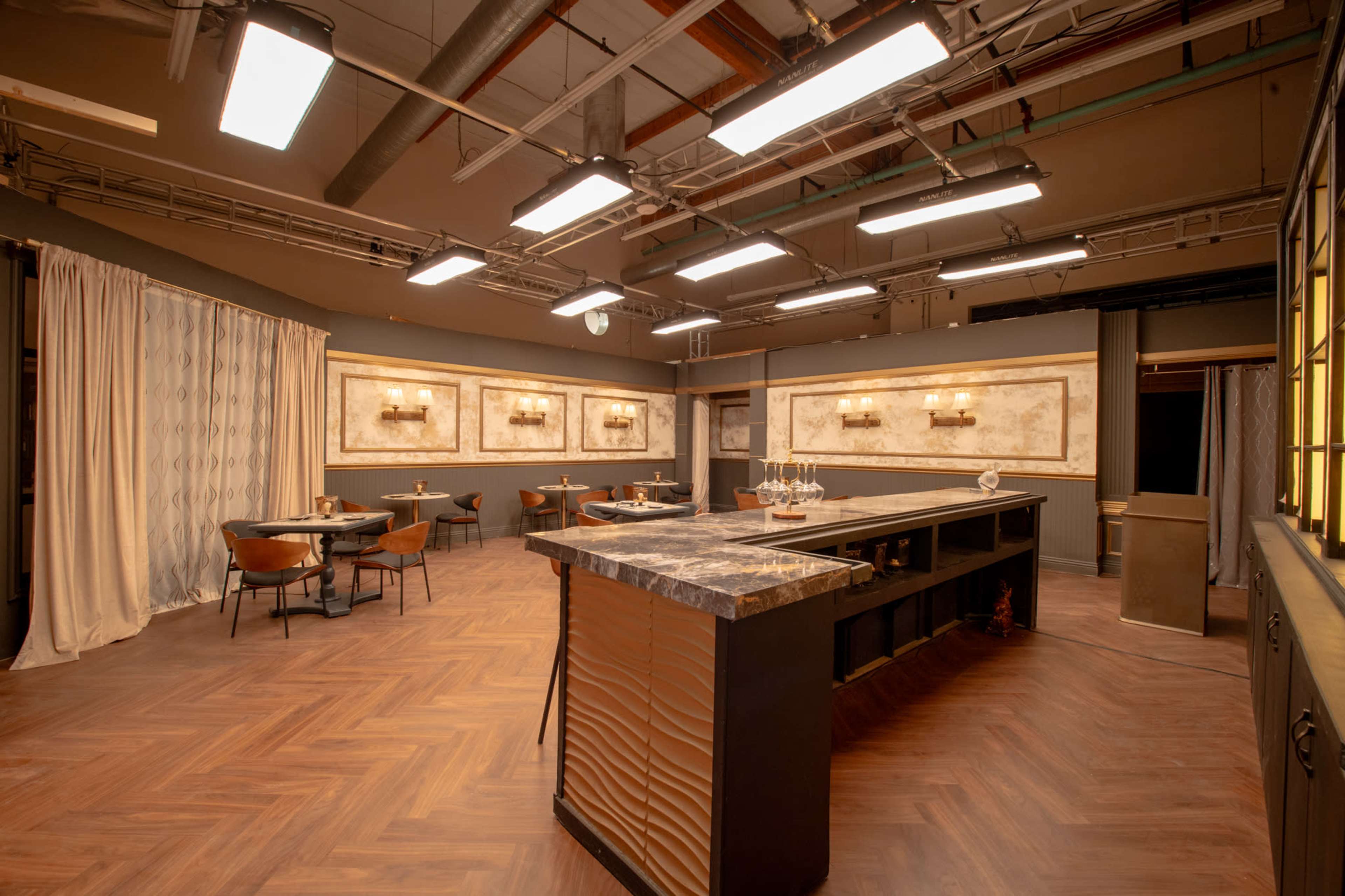 The image shows a spacious dining area with a large island countertop, several tables, and wall-mounted light fixtures illuminating the space.