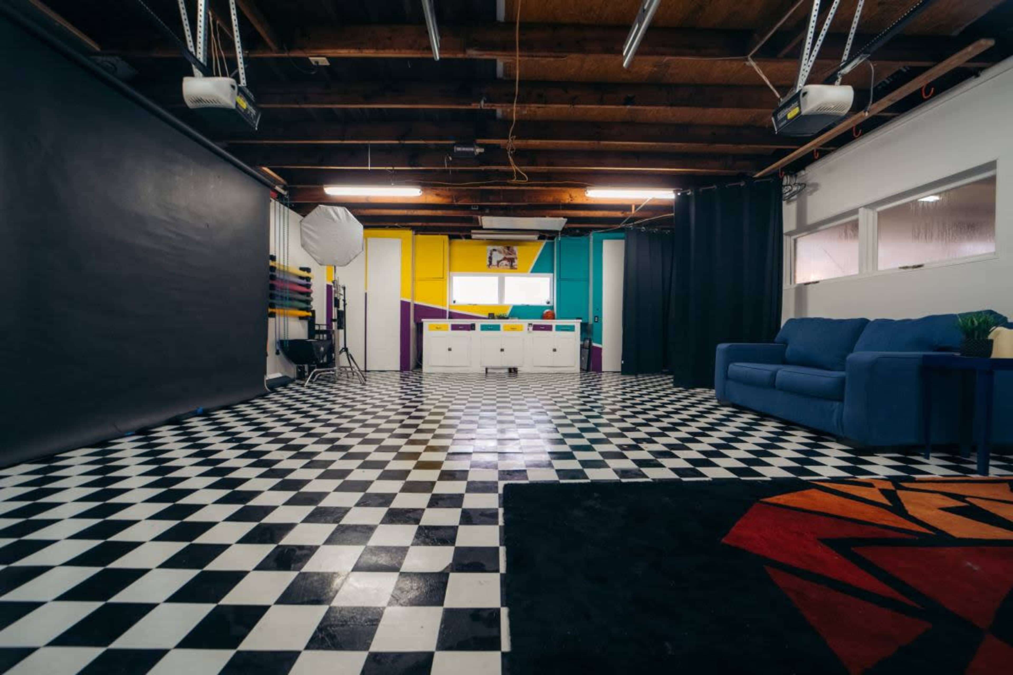 A spacious photography studio with a checkered black and white floor, a blue couch, and a colorful backdrop.