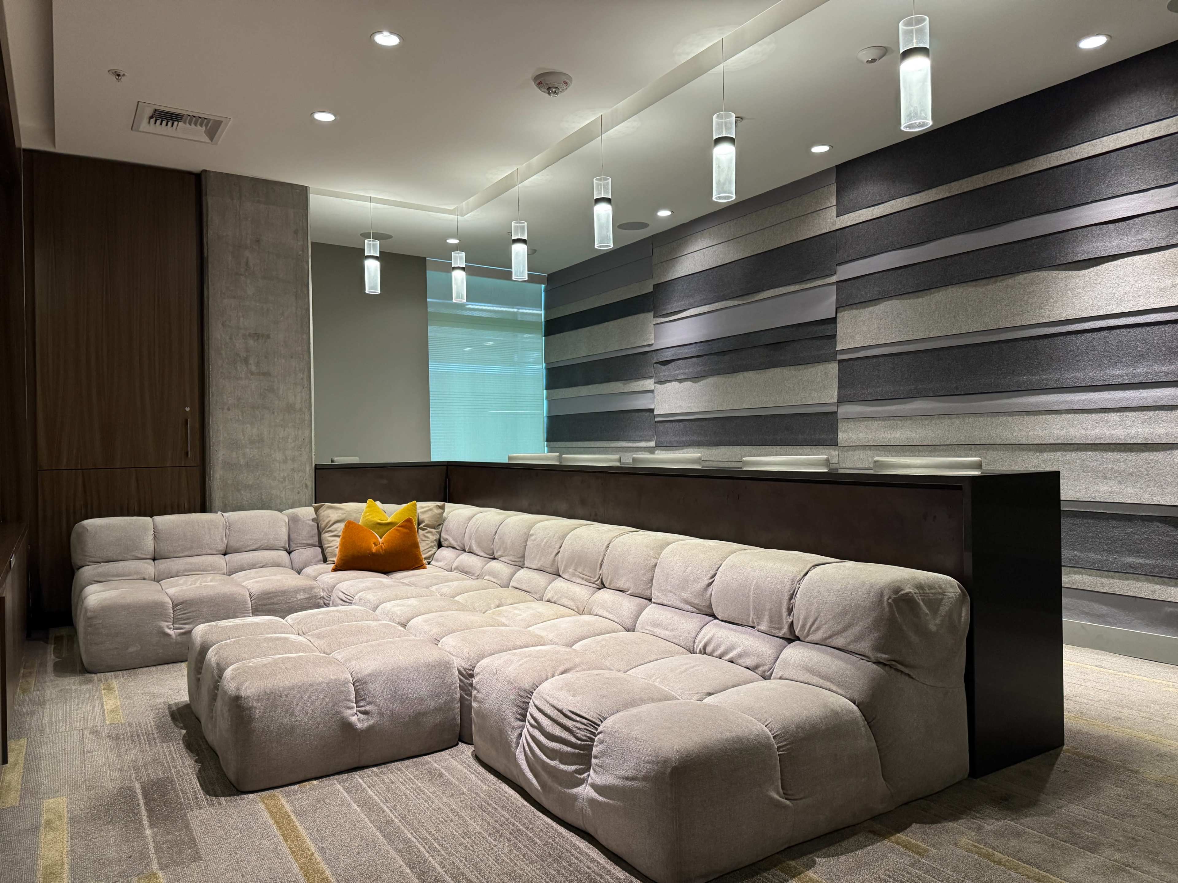 The image shows a modern lounge area featuring a large, modular, light-colored sofa and a textured wall with horizontal stripes in various shades of gray.