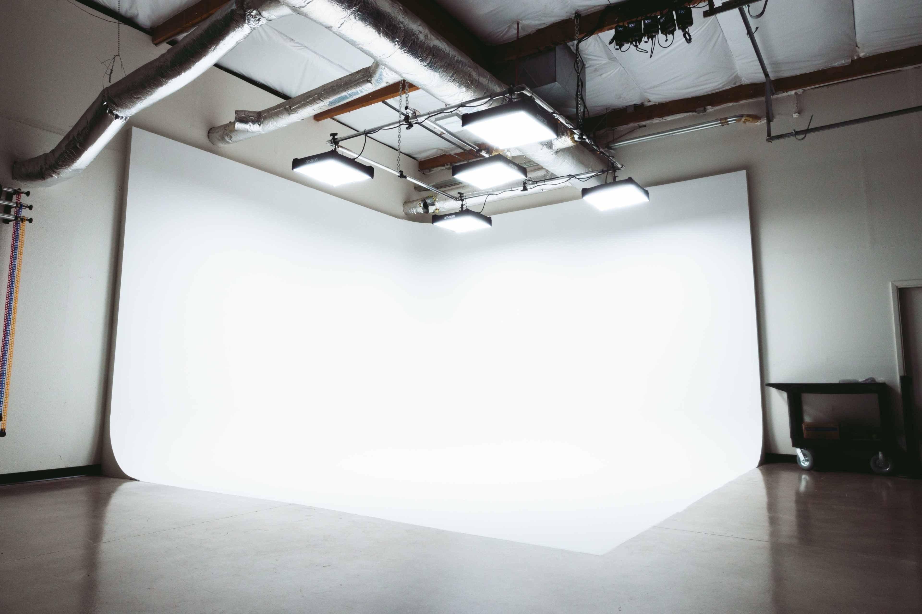 An empty photography studio with a seamless white backdrop and overhead lighting.