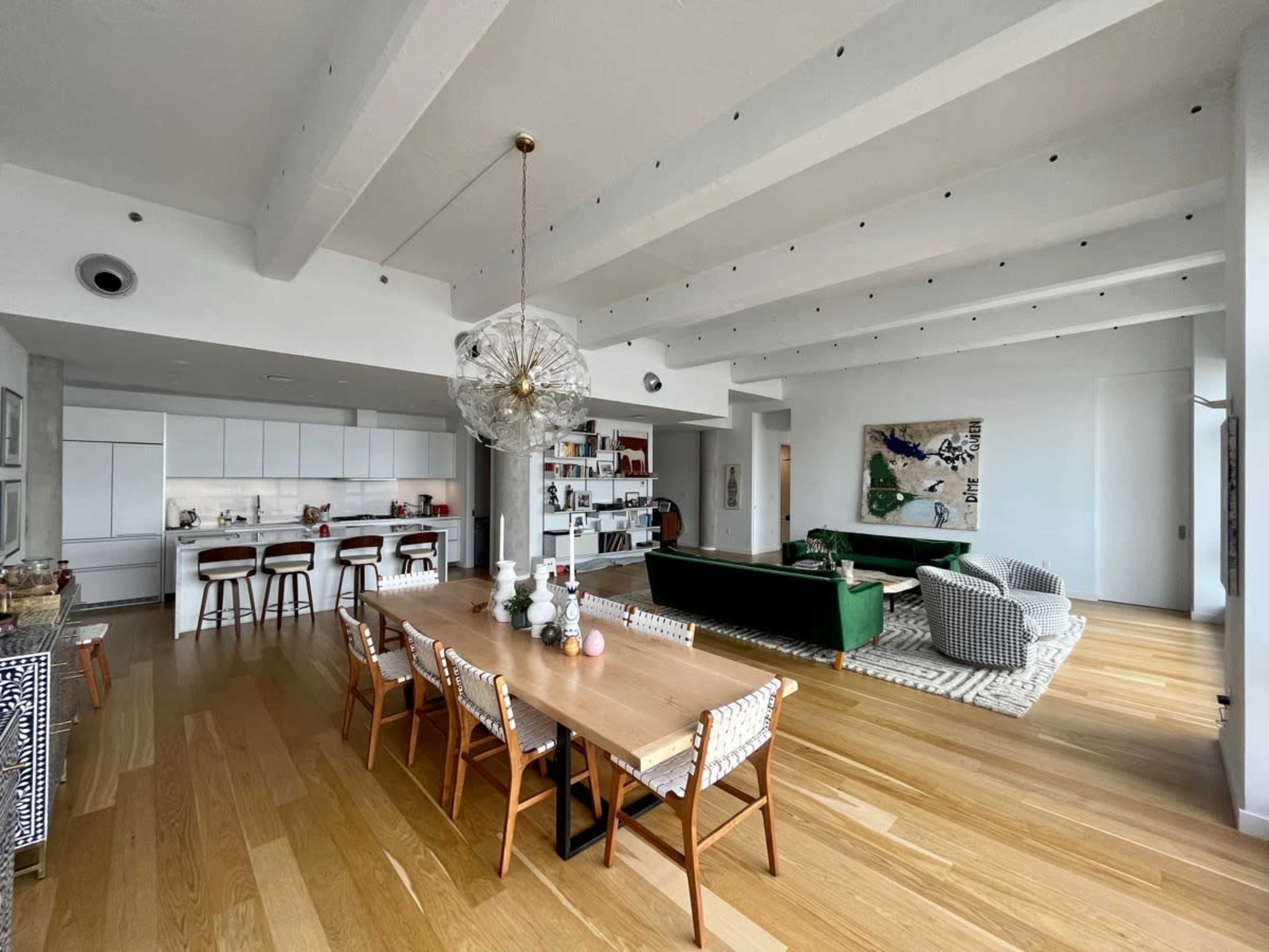 A modern, open-concept living space with a dining table, kitchen area, and living room featuring green sofas.