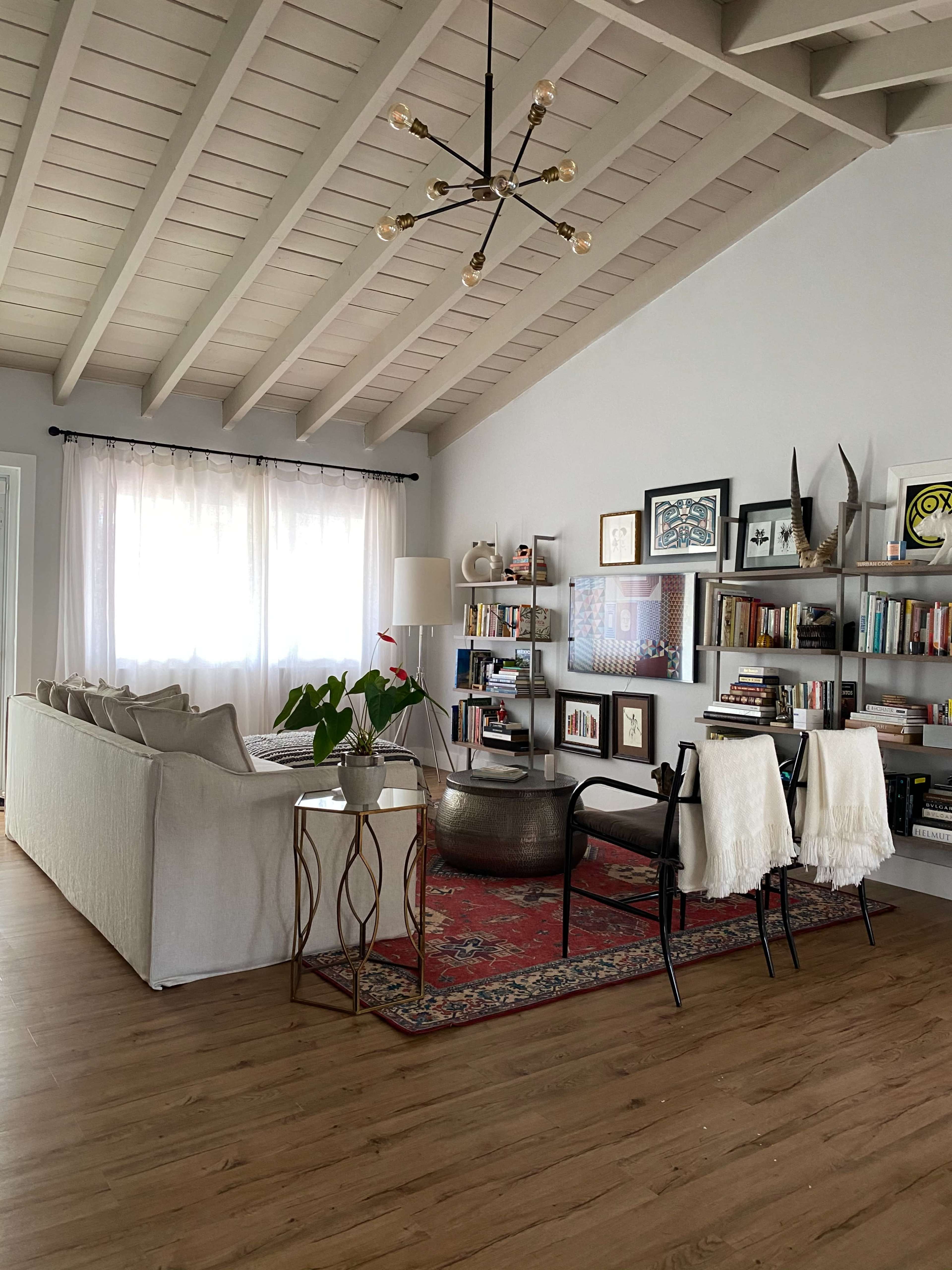 A modern living room with a light-colored sofa, a round coffee table, bookshelves, and a patterned area rug under a chandelier.