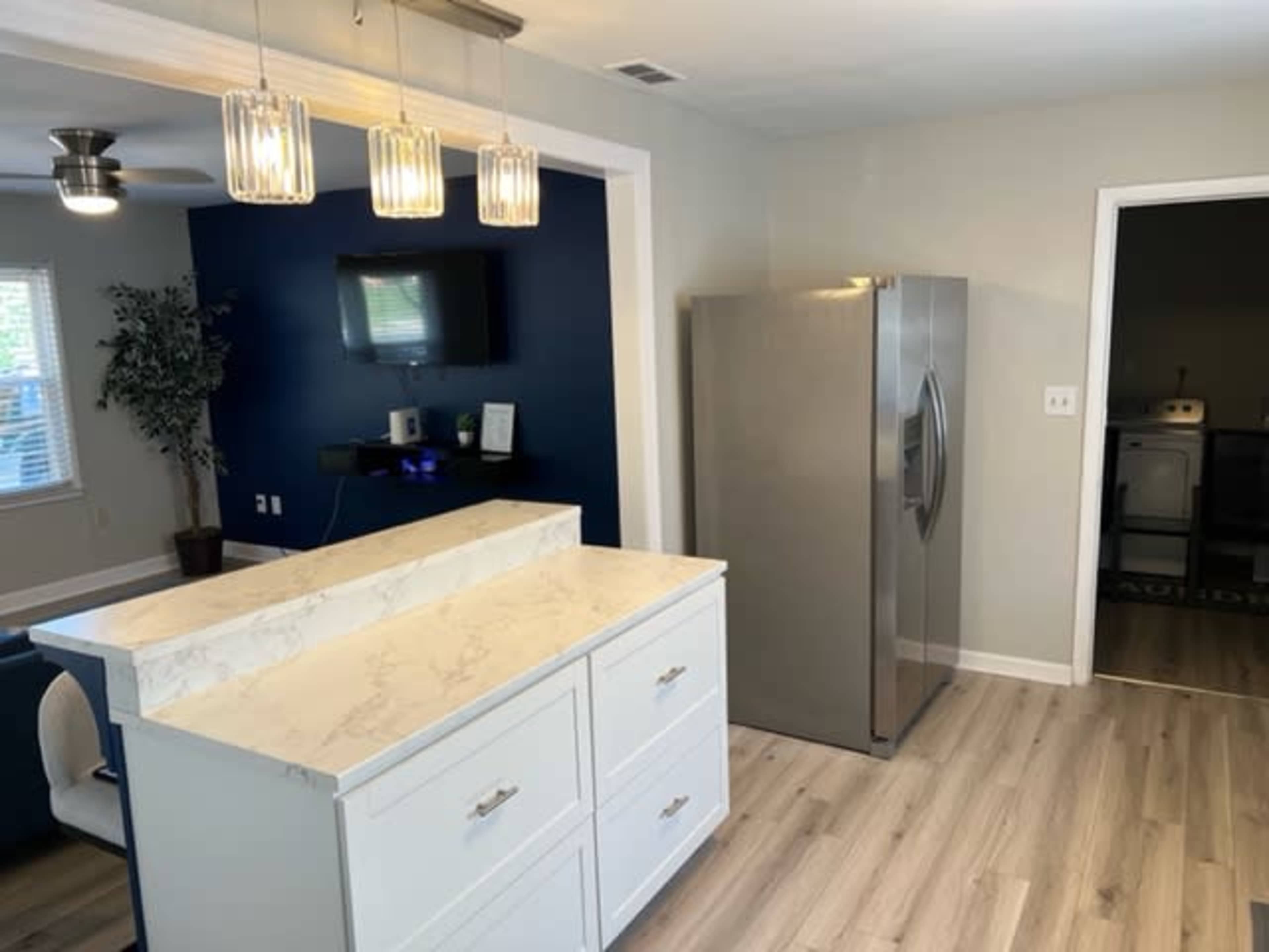 A modern kitchen with a central island, stainless steel refrigerator, and a dark blue accent wall.