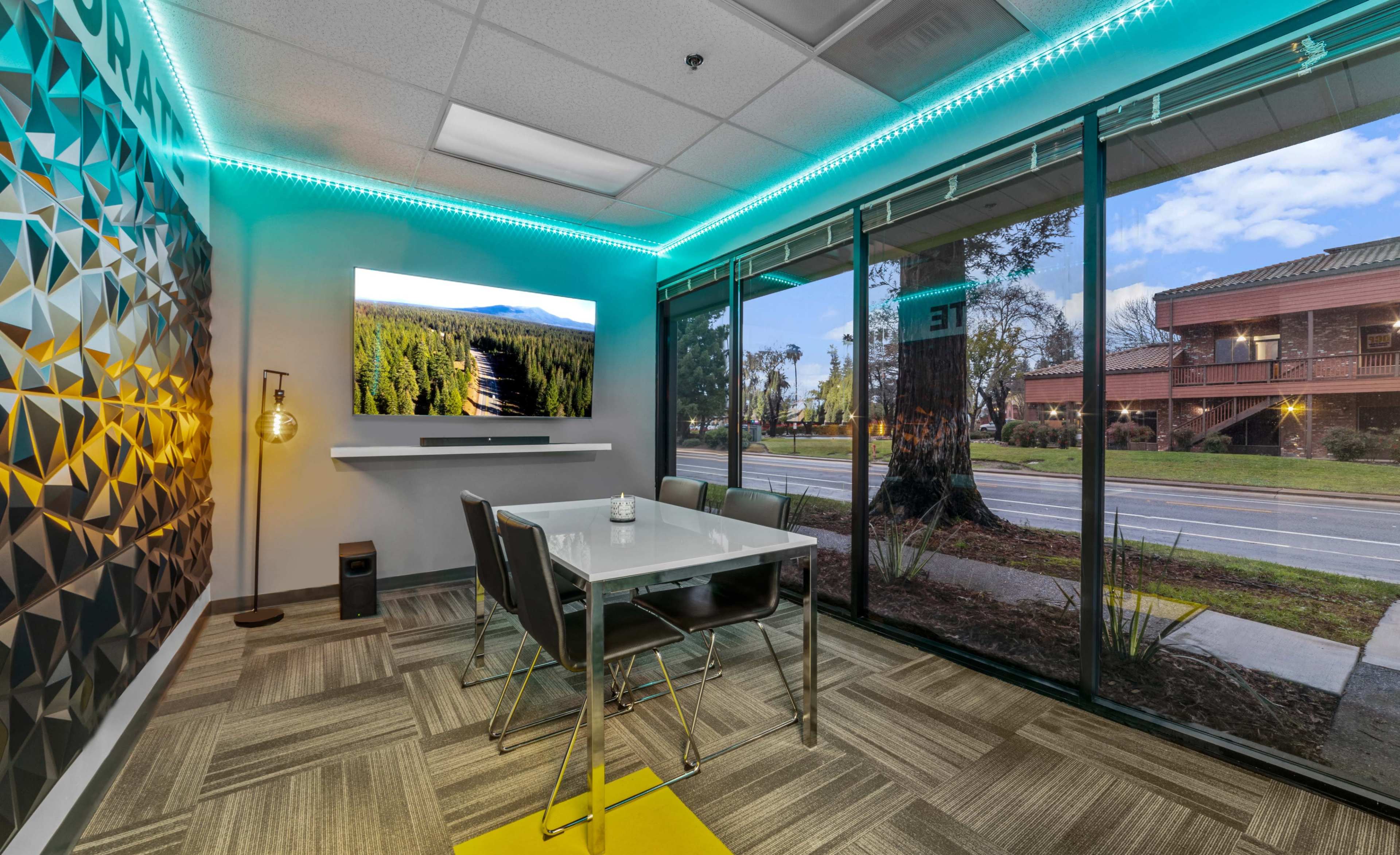 A modern conference room features a glass wall with a view of the street, a large screen displaying a nature scene, and a table surrounded by chairs.