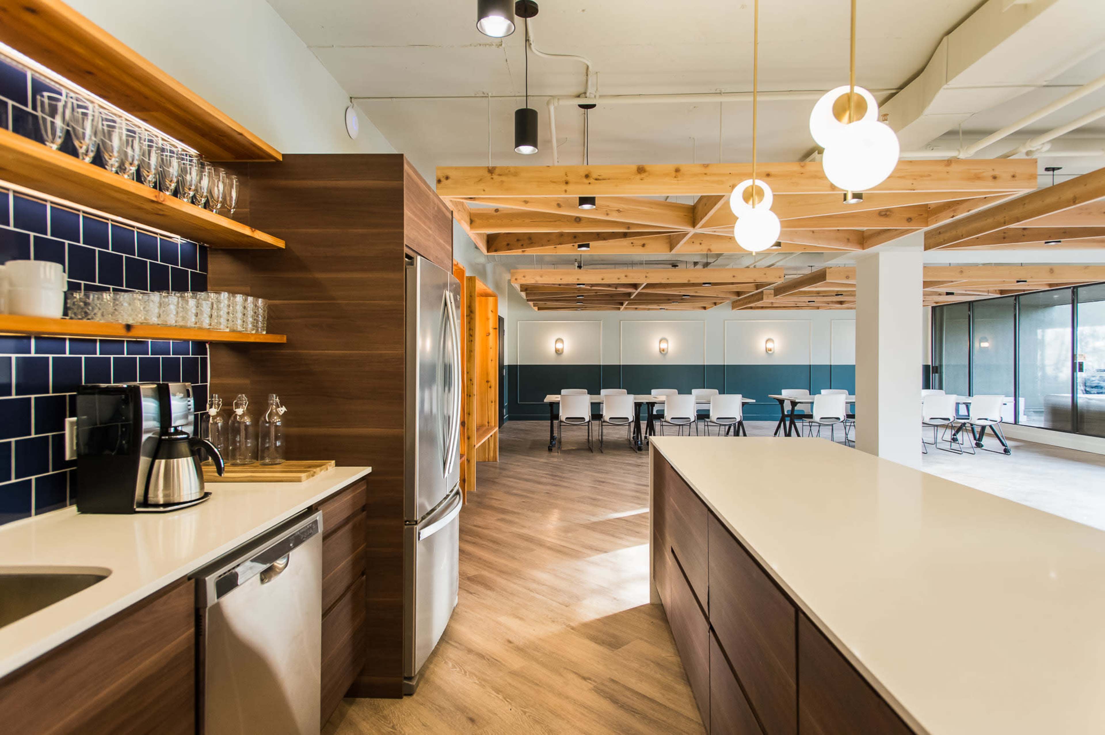 A modern kitchen and dining area with wooden ceiling beams, a blue tiled backsplash, and a spacious seating arrangement.