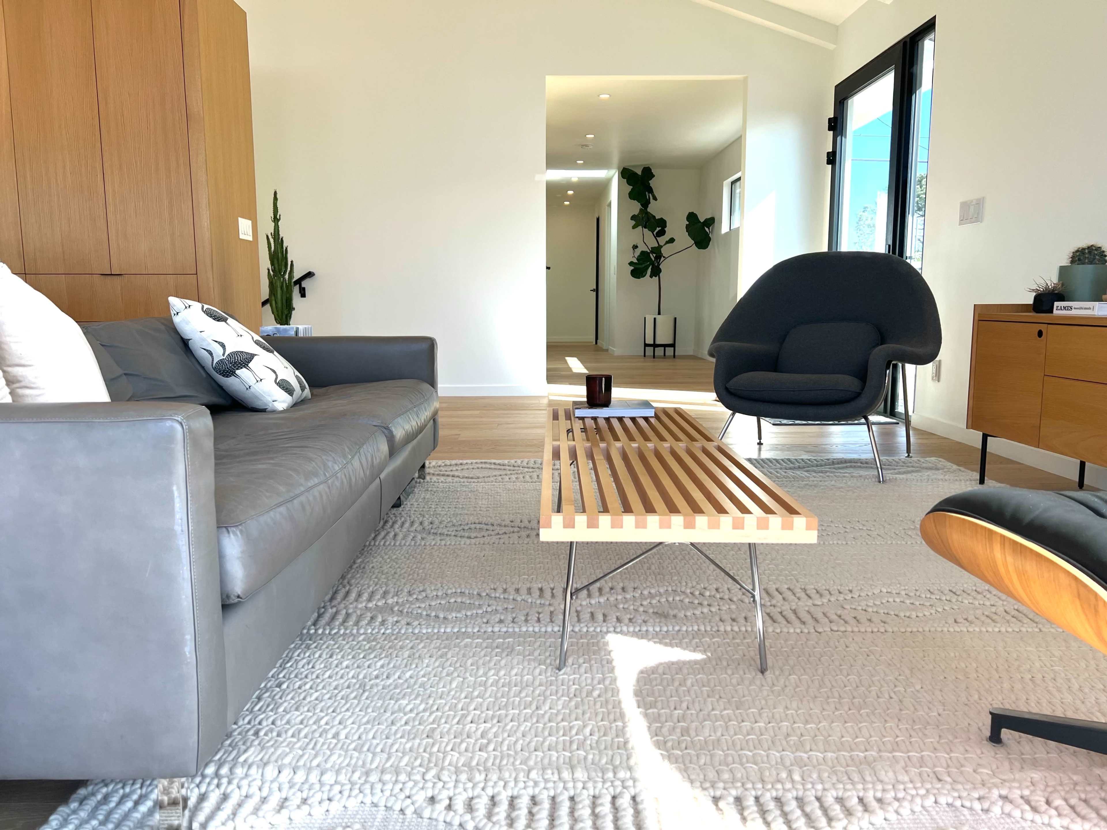 The scene features a modern living room with a gray sofa, a wooden coffee table, and an armchair, all set against a bright, minimalist backdrop.