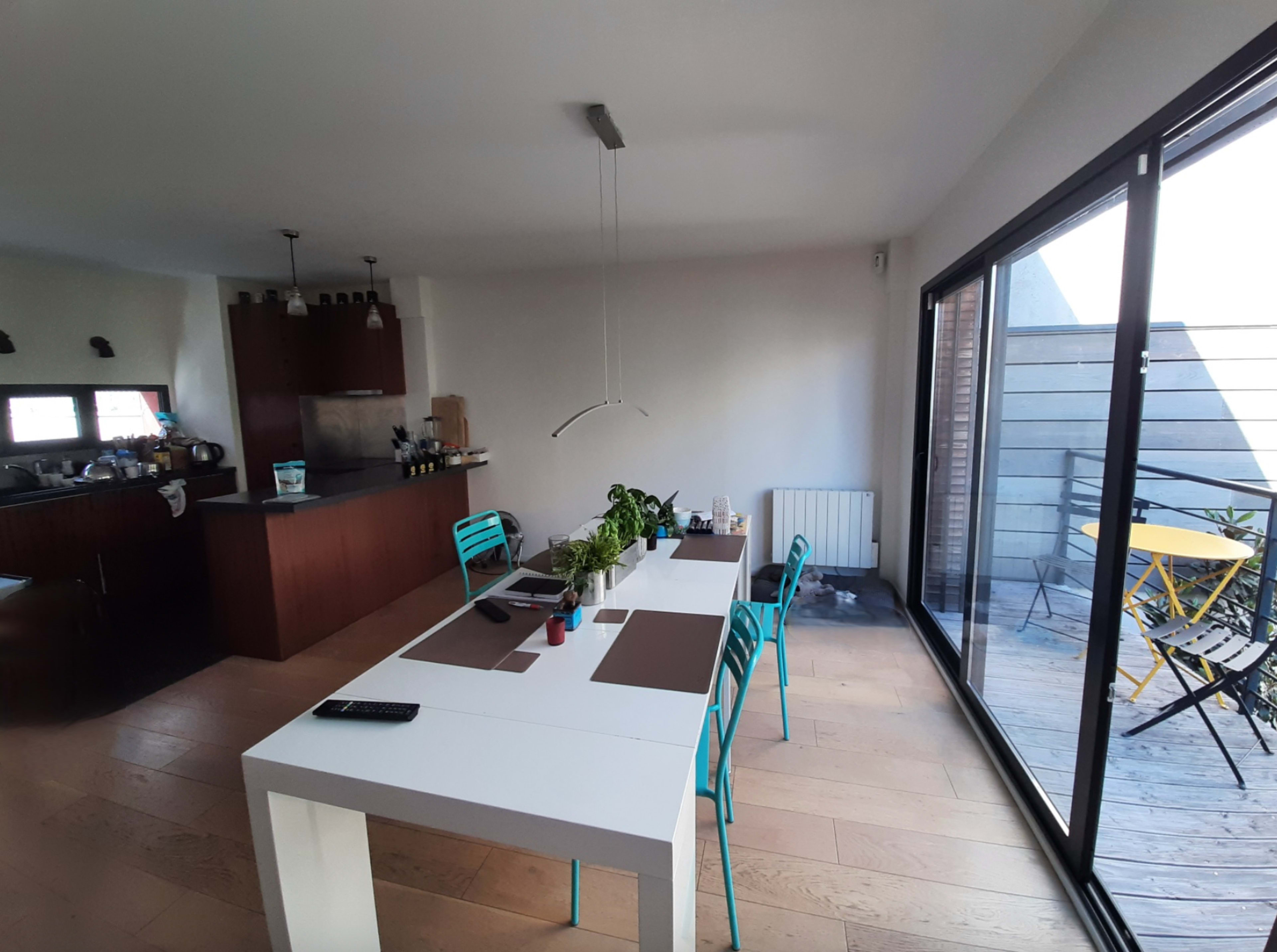 A modern kitchen and dining area with a white table, blue chairs, and a sliding glass door leading to a balcony.