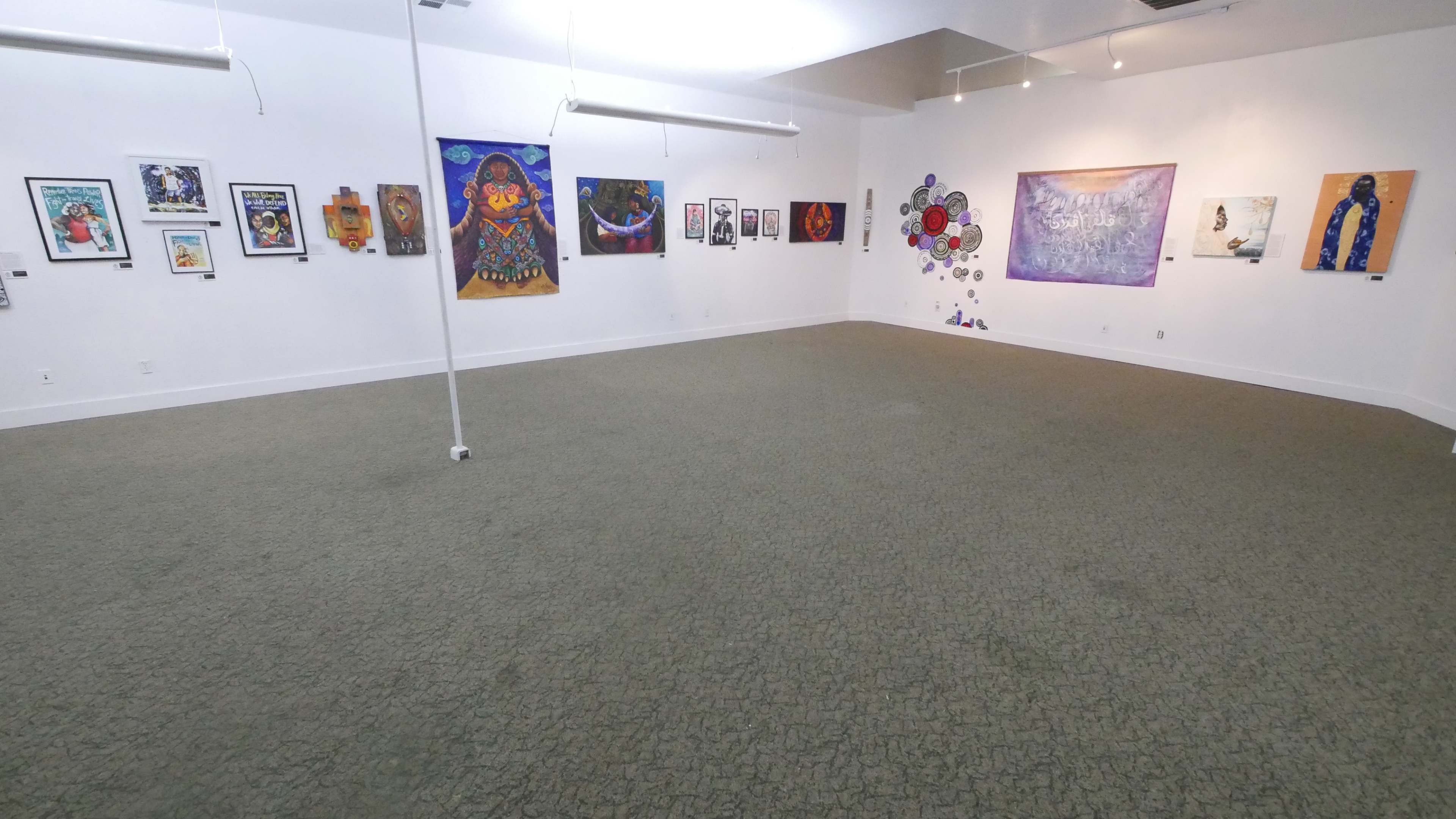 A spacious art gallery with various framed artworks displayed on the walls, and a clear carpeted floor in the center.
