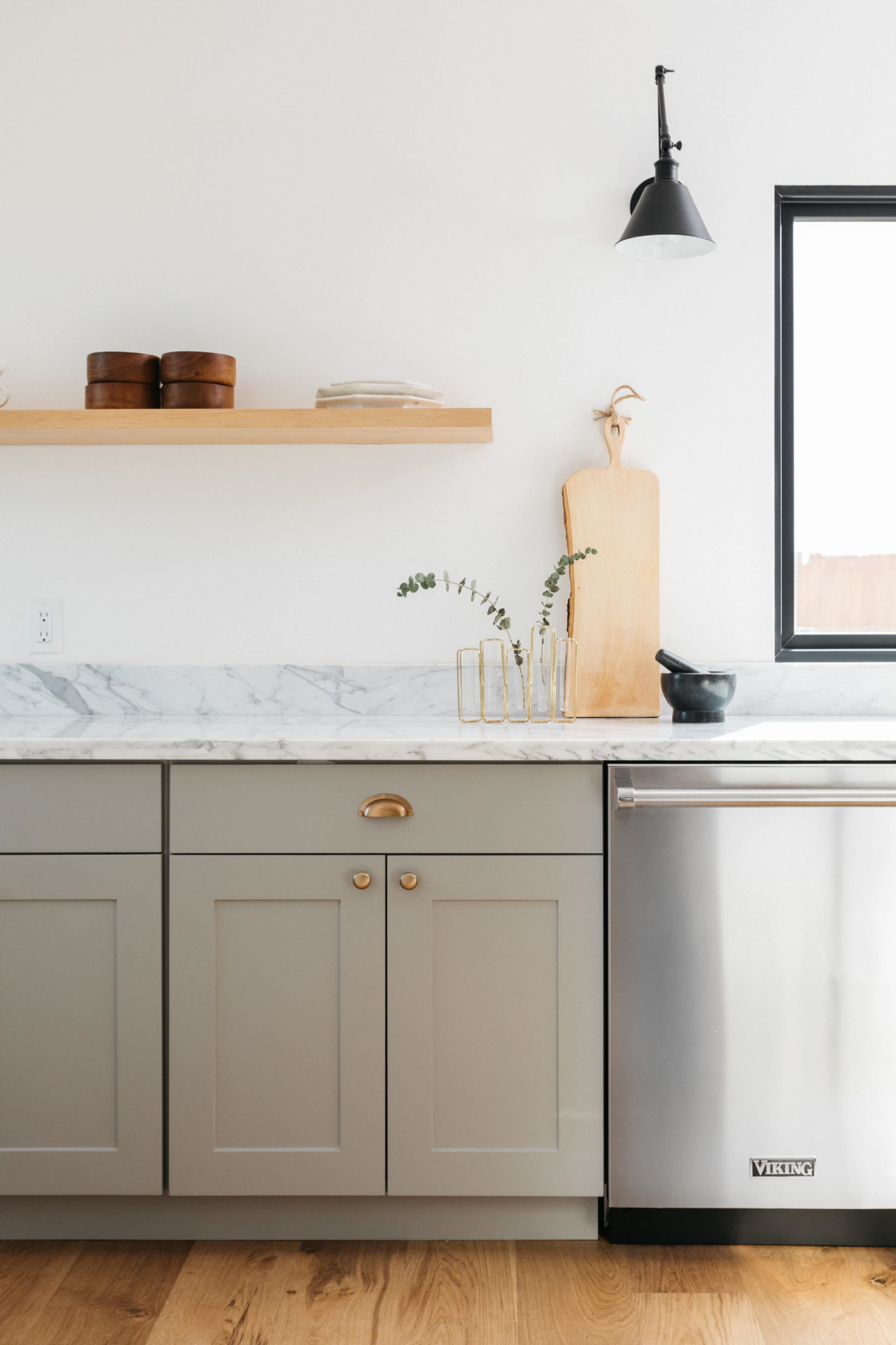 A modern kitchen featuring gray cabinets, a marble countertop, and stainless steel appliances, with wooden shelves displaying decorative items.