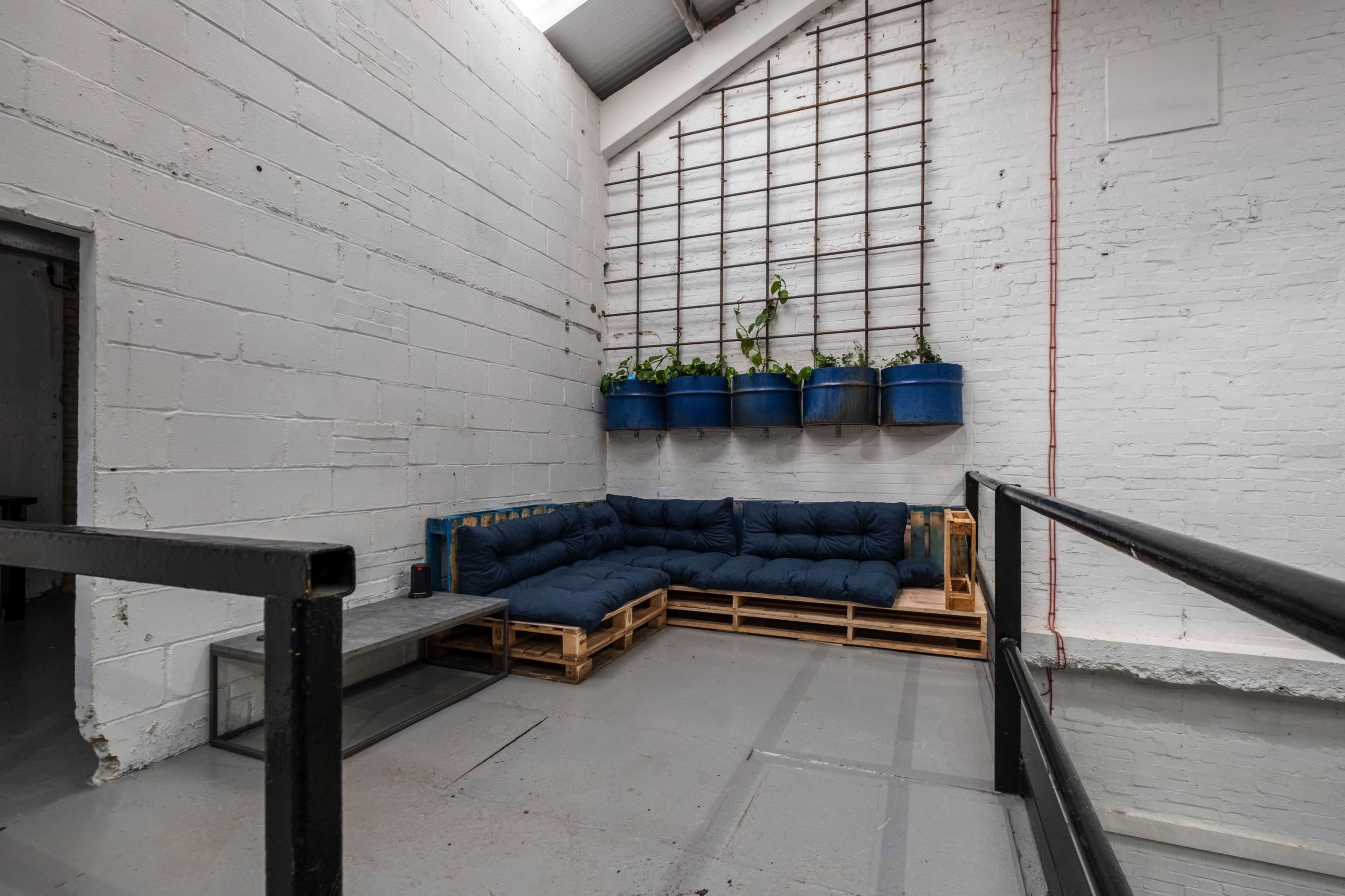 A seating area with a blue pallet sofa against a white brick wall, complemented by hanging planters on a grid structure above.