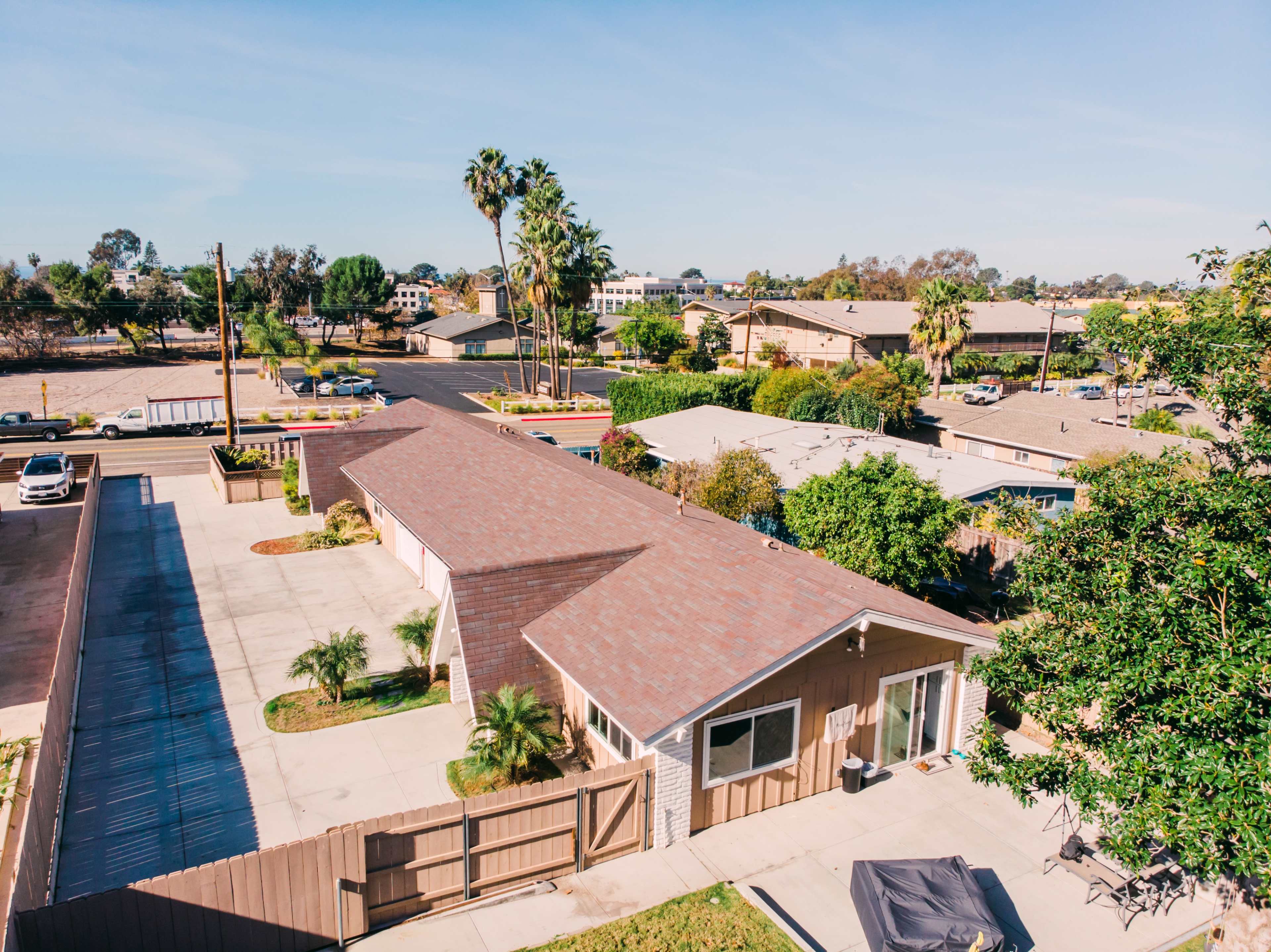 The image shows a residential area with single-story houses, palm trees, and parking spaces, viewed from an elevated angle.