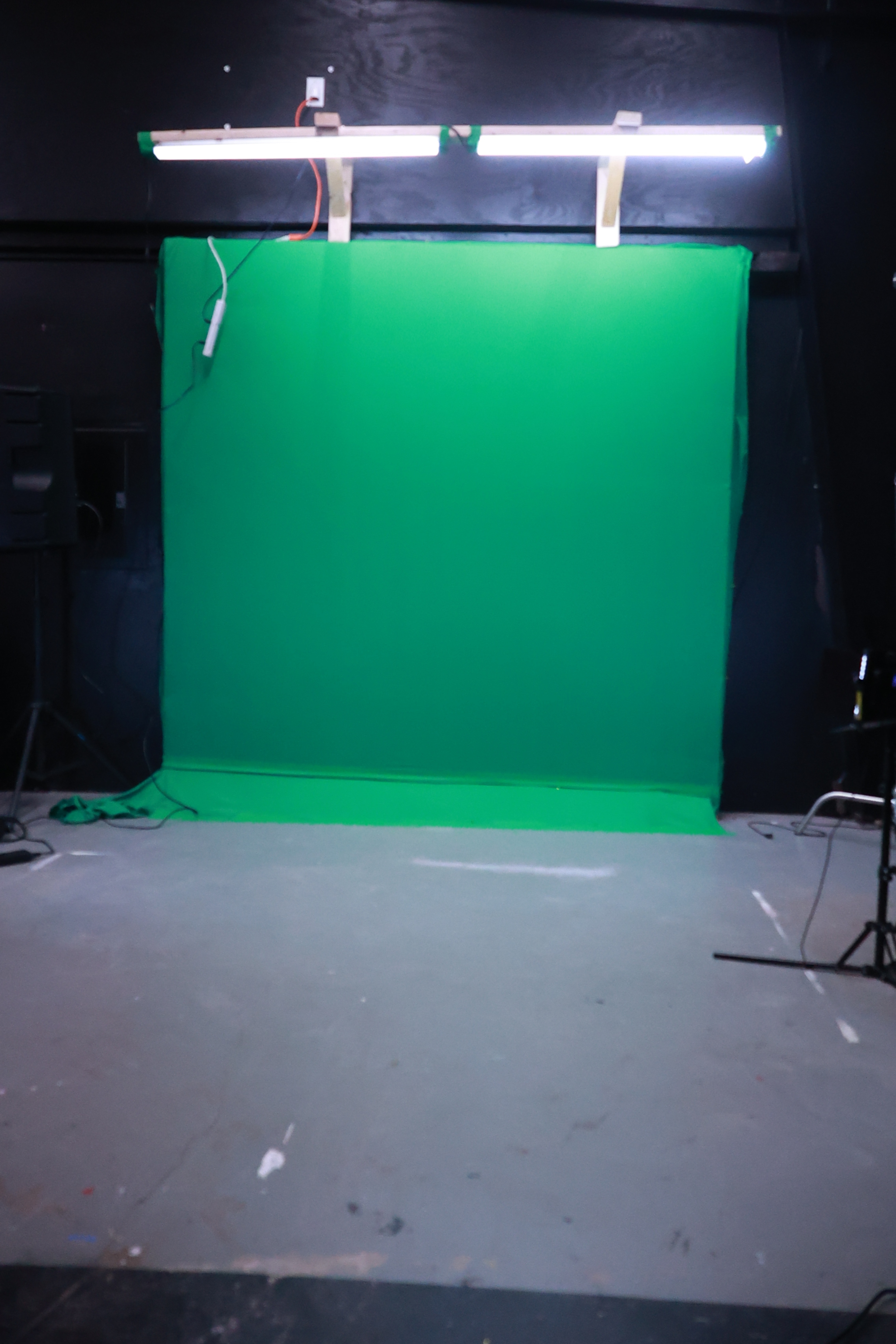 A green screen setup in a studio with overhead lights and an empty space in front.