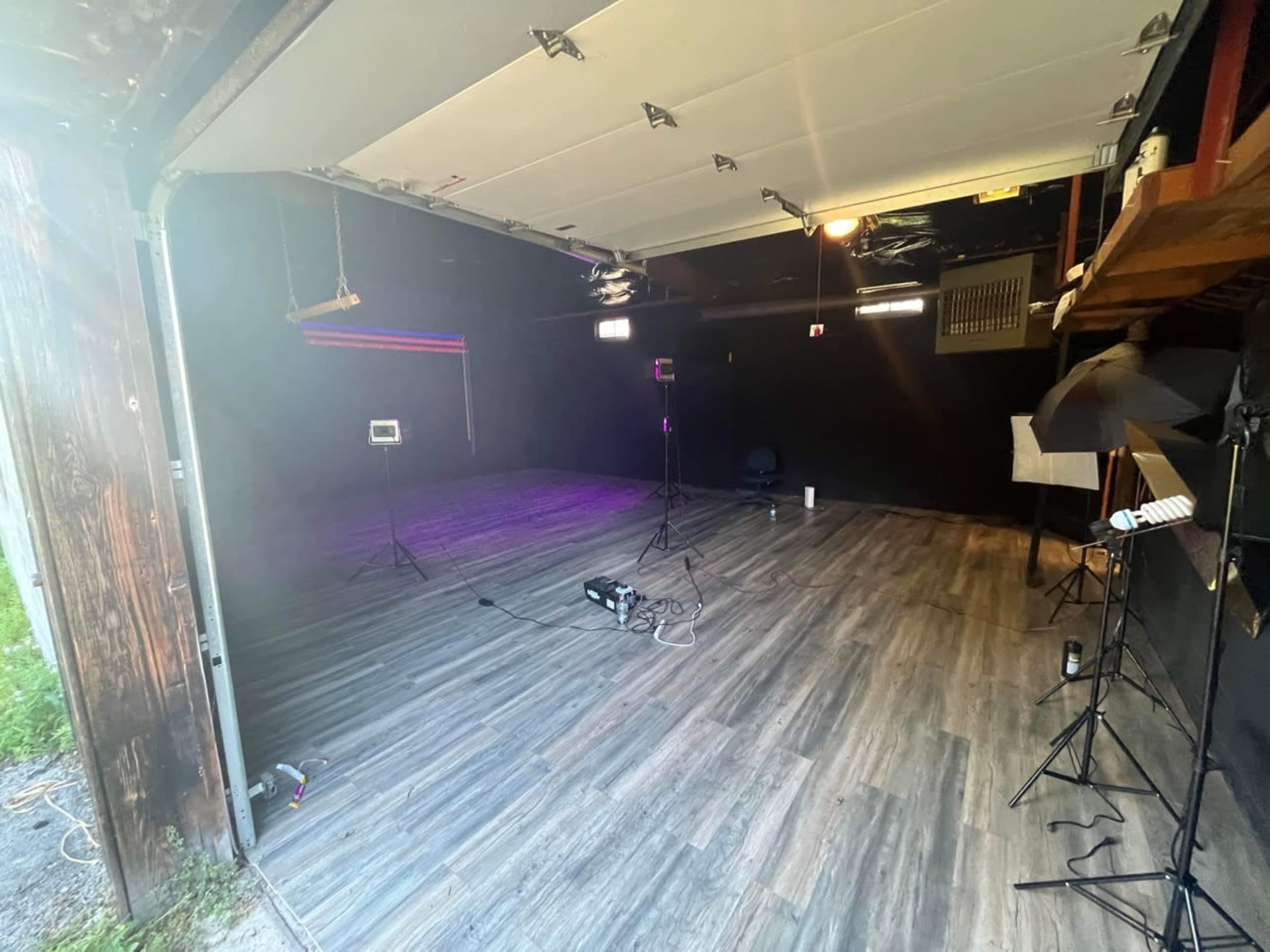 A spacious, empty room with black walls, wooden flooring, and multiple lights set up for a photography or video shoot.