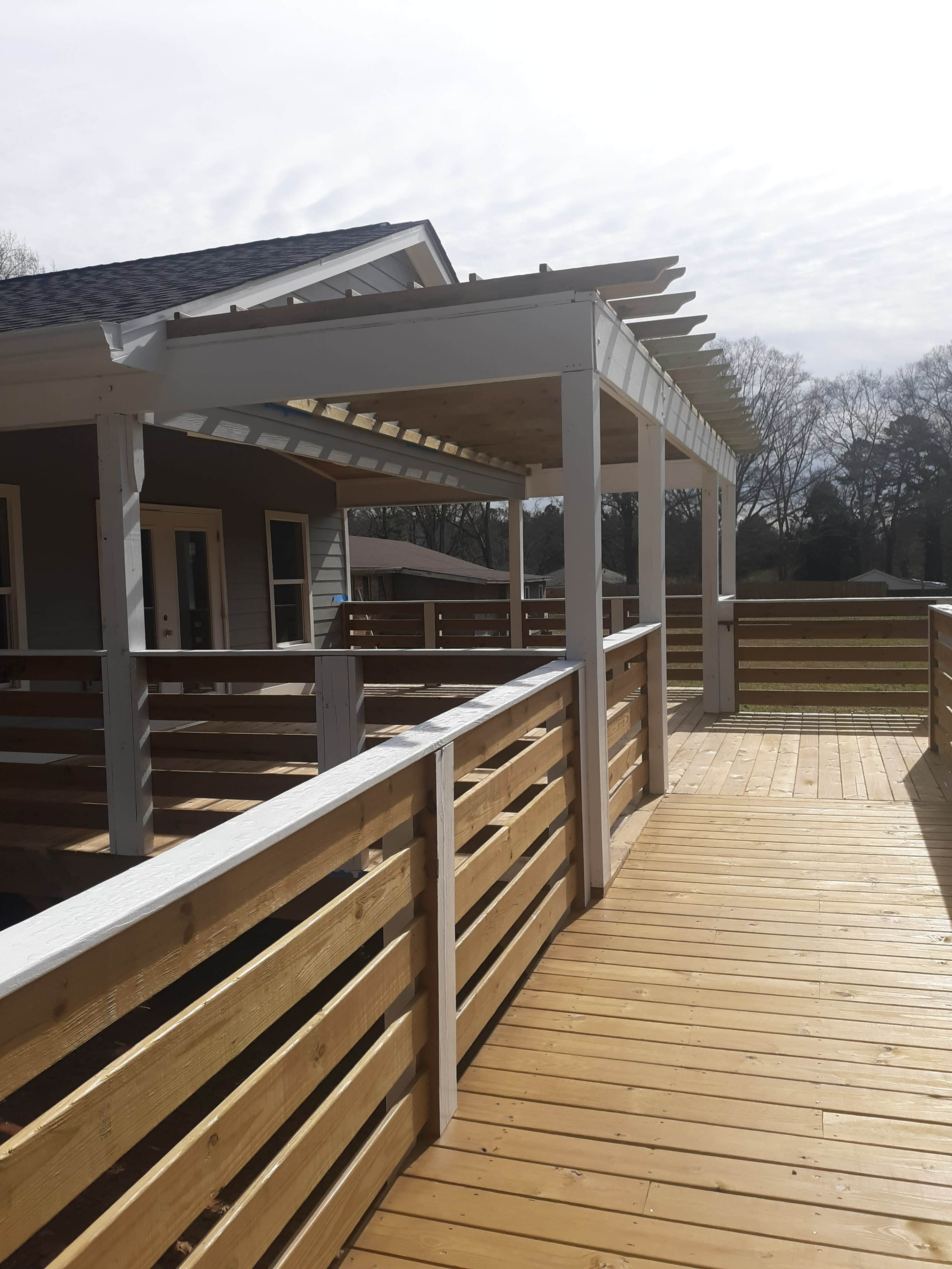 A wooden deck with a covered pergola, leading to a house with a gray exterior.