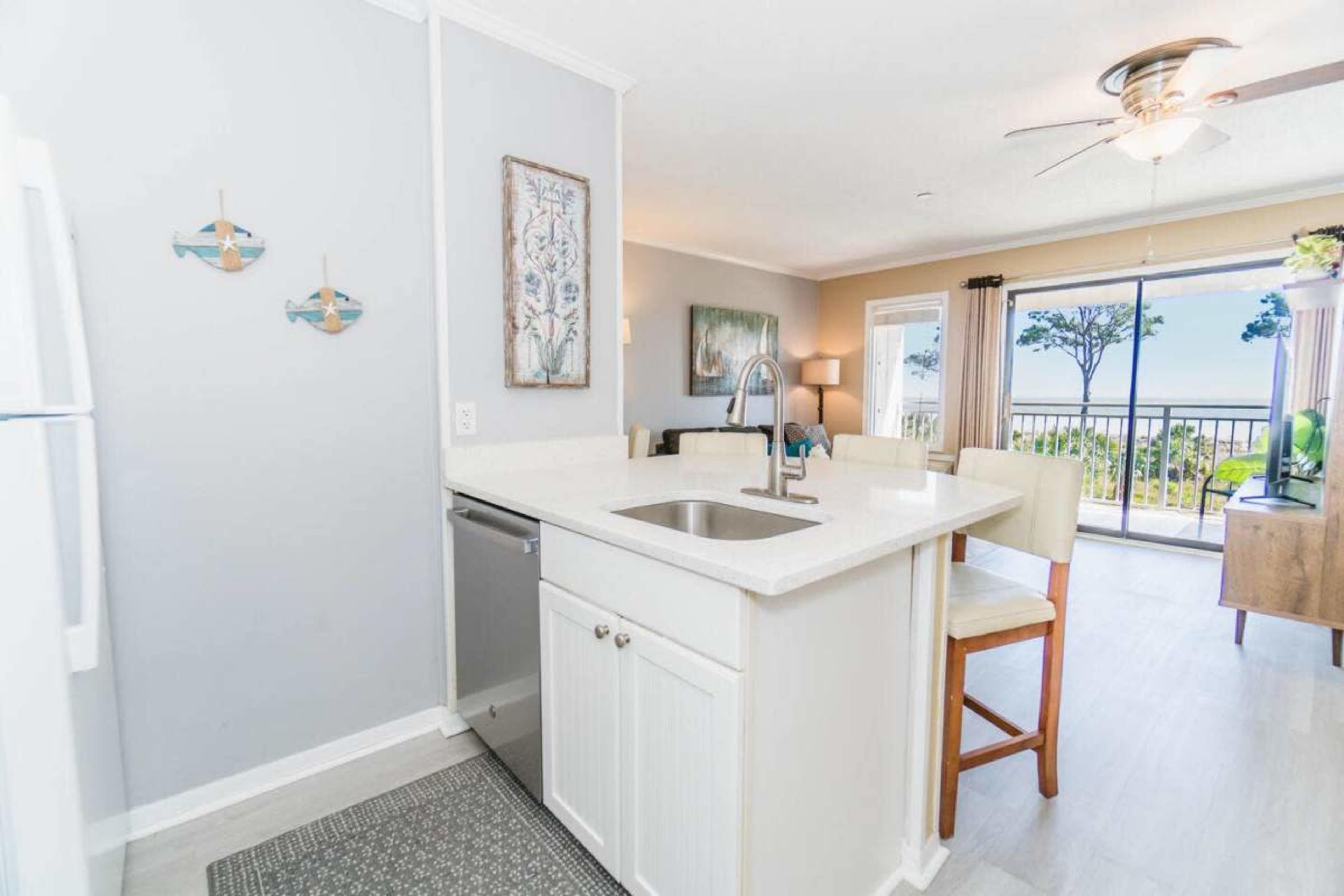 The image shows a modern kitchen area with white cabinetry and a view of a balcony through a sliding glass door.