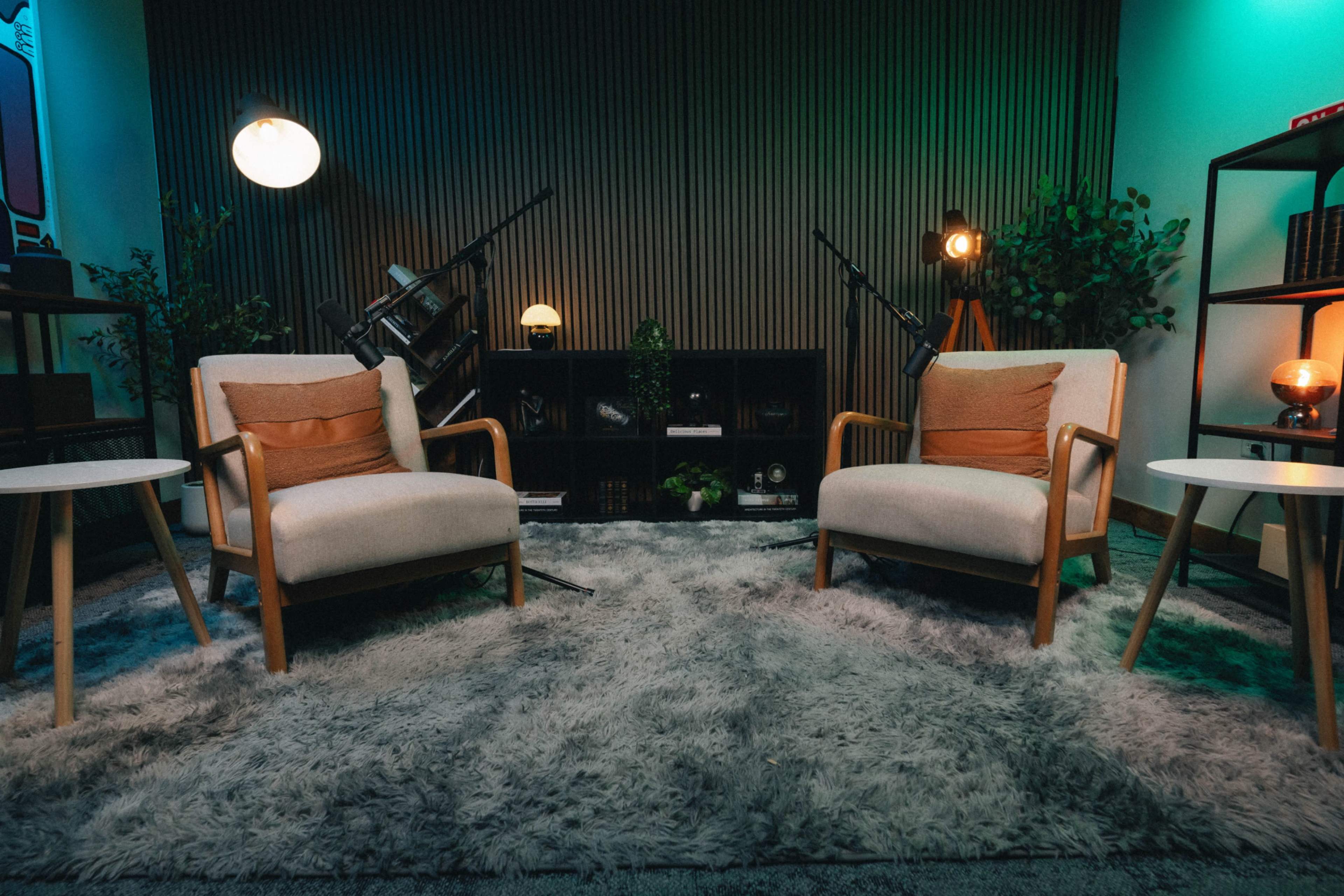 The image depicts a cozy indoor setting with two armchairs facing each other on a plush rug, surrounded by decorative plants and soft lighting.