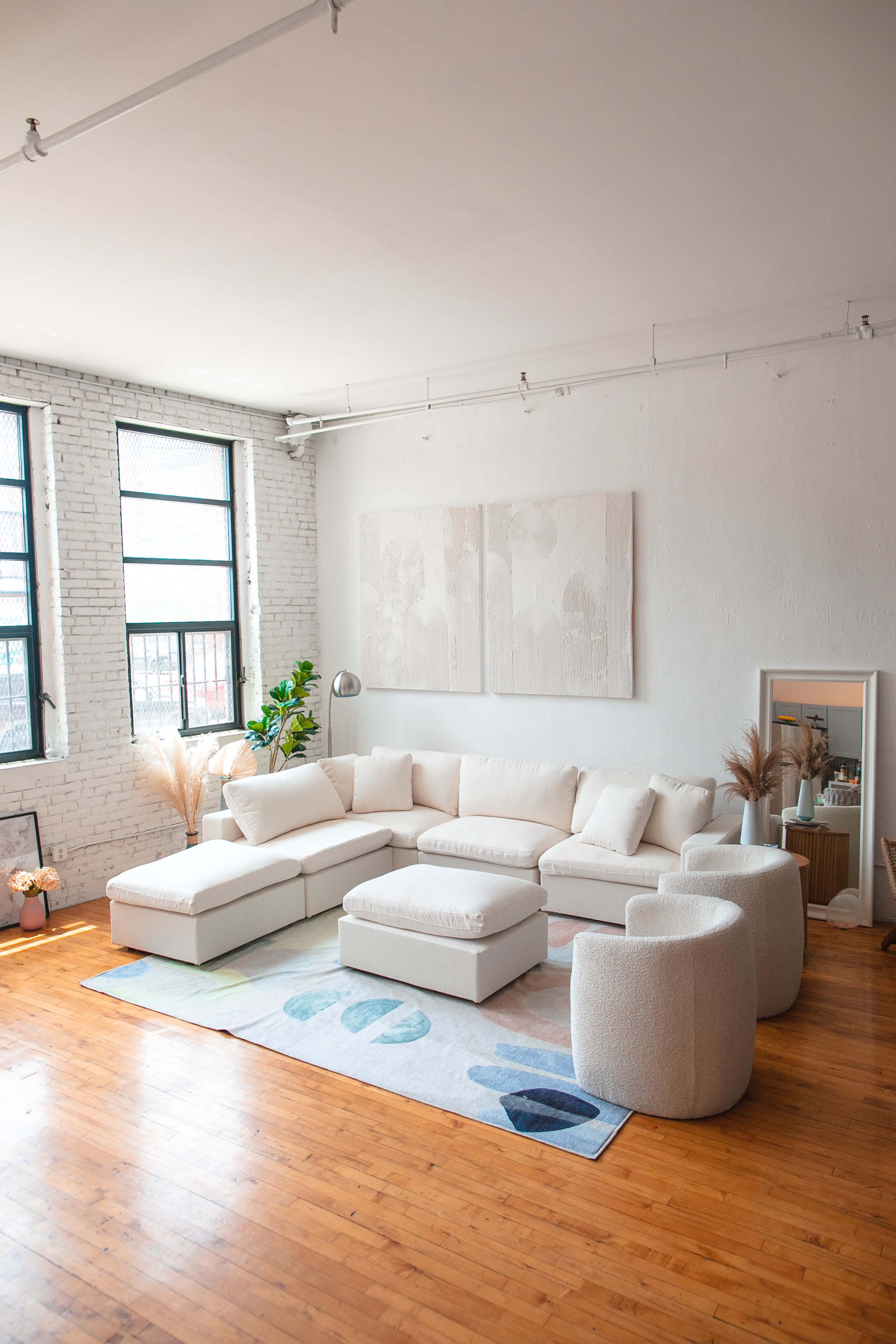 A bright living room with a large white sectional sofa, a round coffee table, and a colorful area rug on wooden flooring.