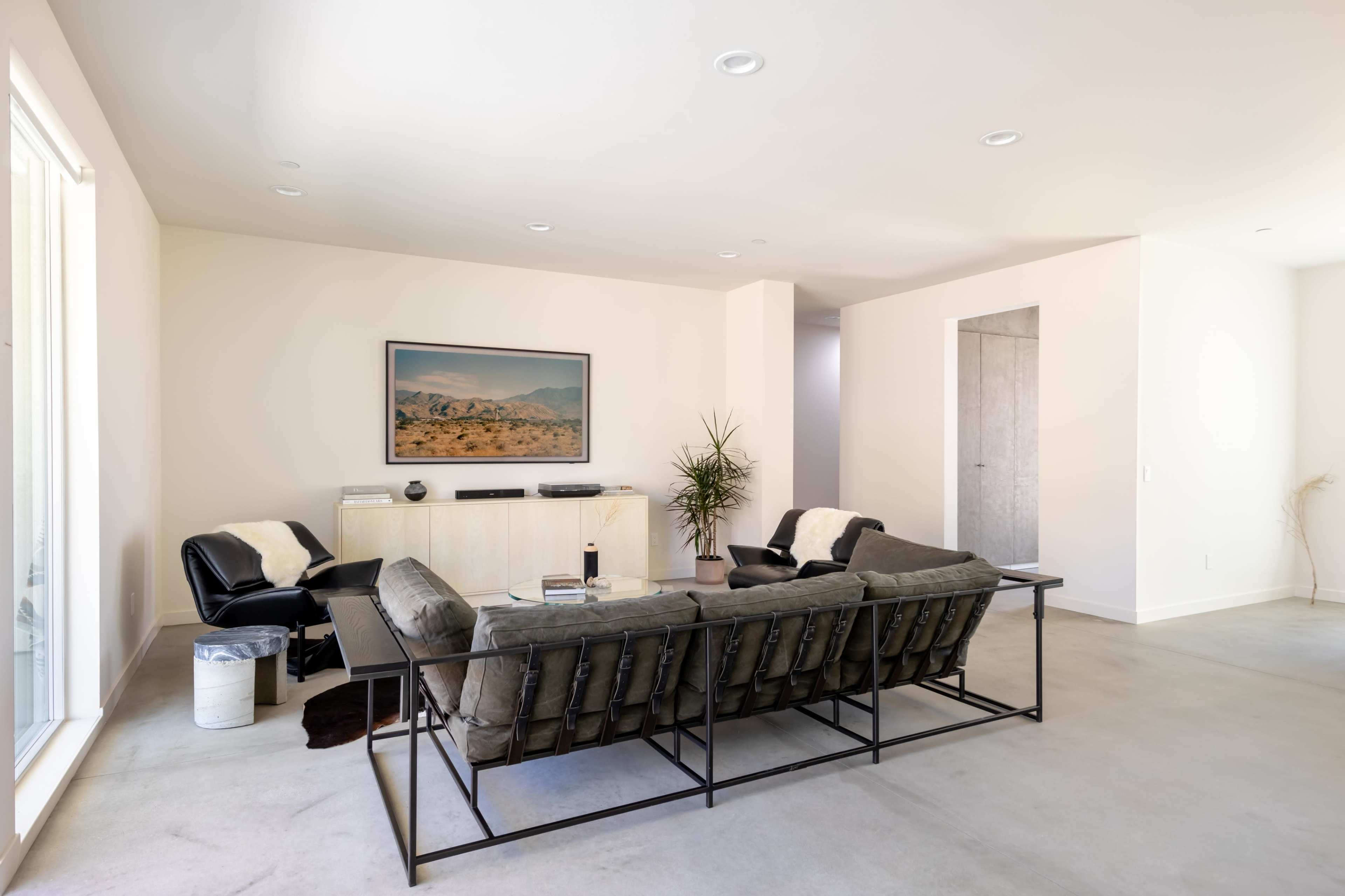 A spacious, modern living room with a black sofa, a coffee table, and a wall-mounted landscape painting.