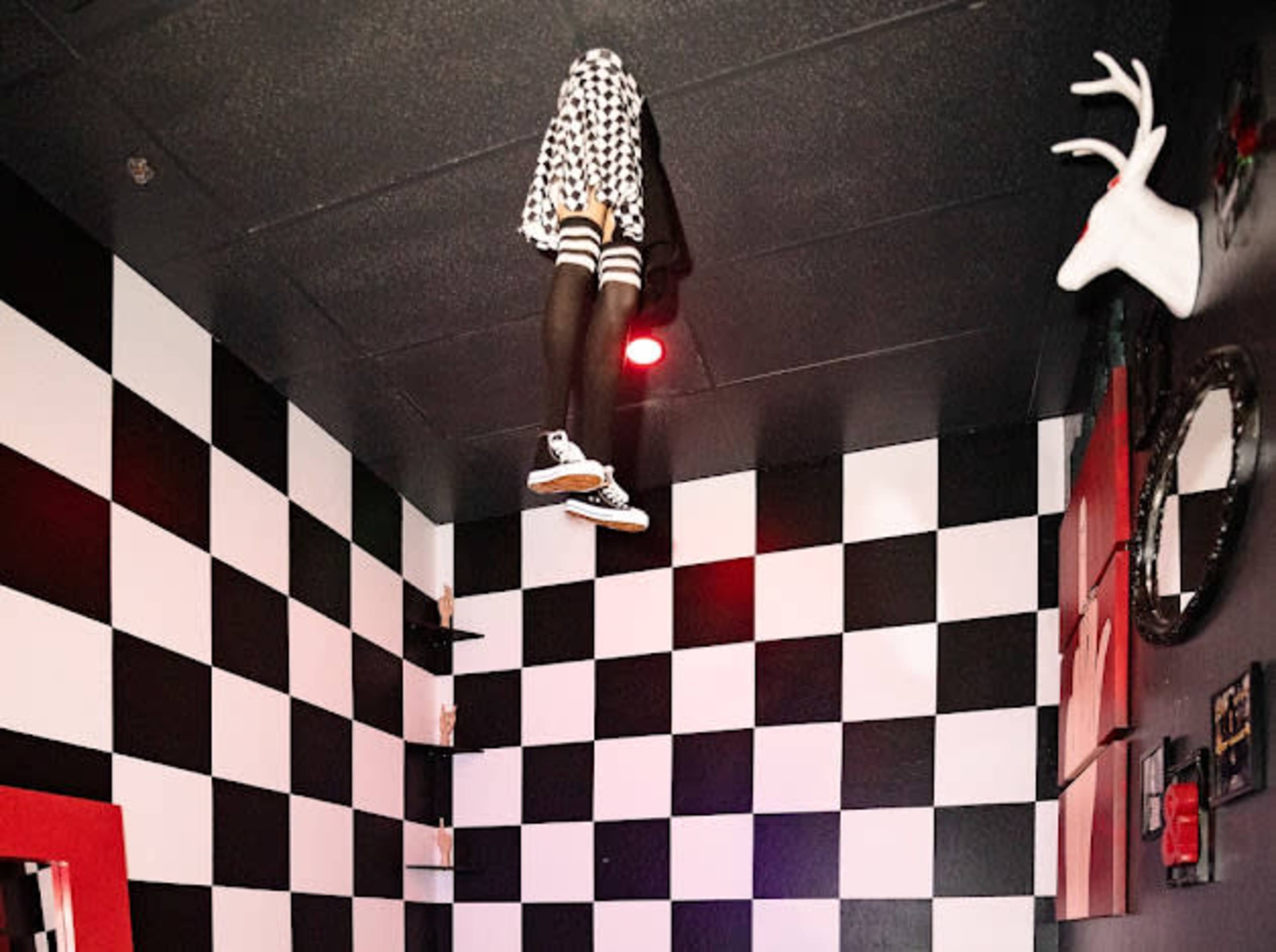 A checkered room features a mannequin dressed in a black and white outfit hanging upside down from the ceiling.