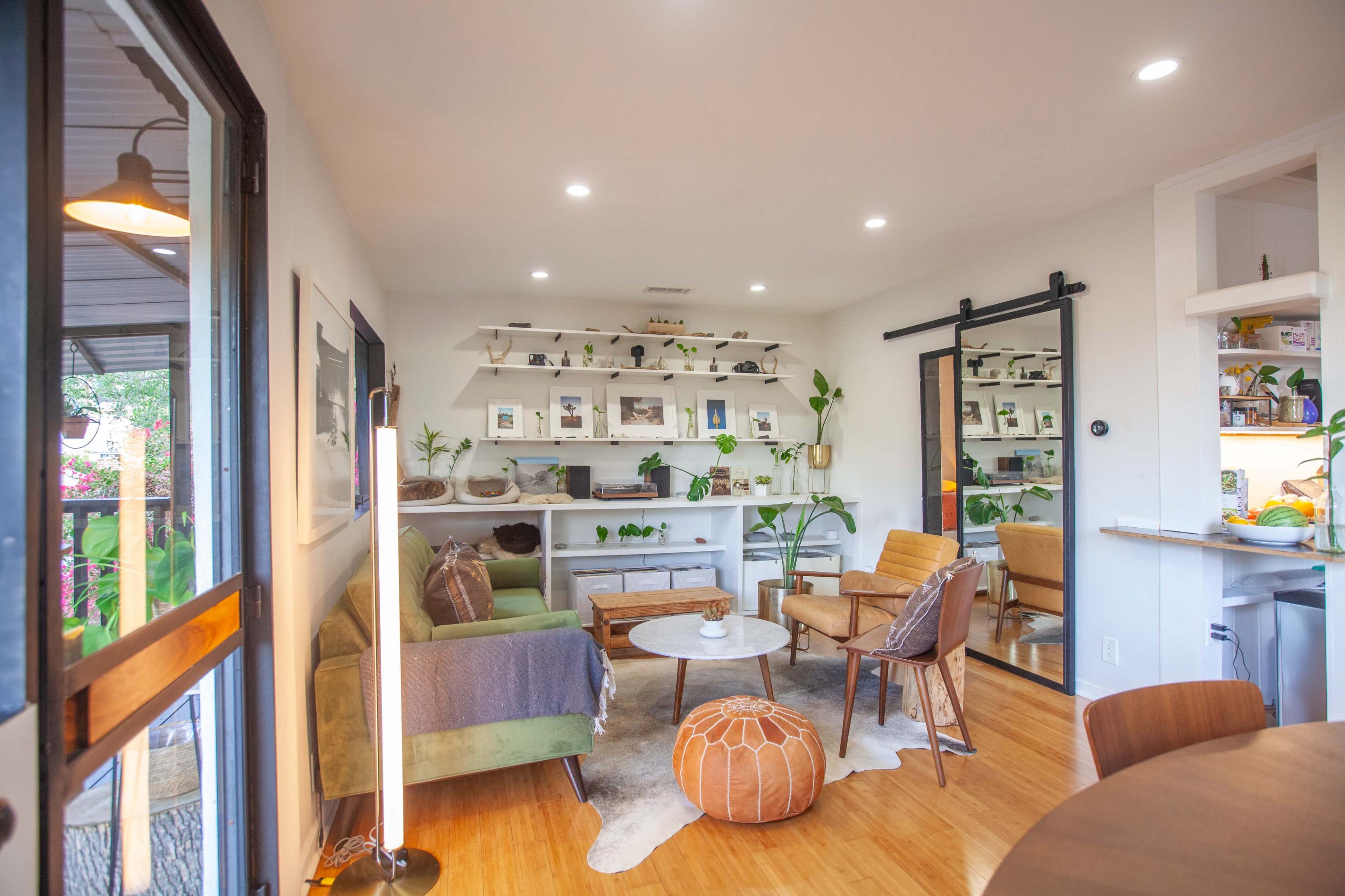A cozy living room with green and brown furniture, a circular coffee table, and a shelf adorned with plants and decorative items.