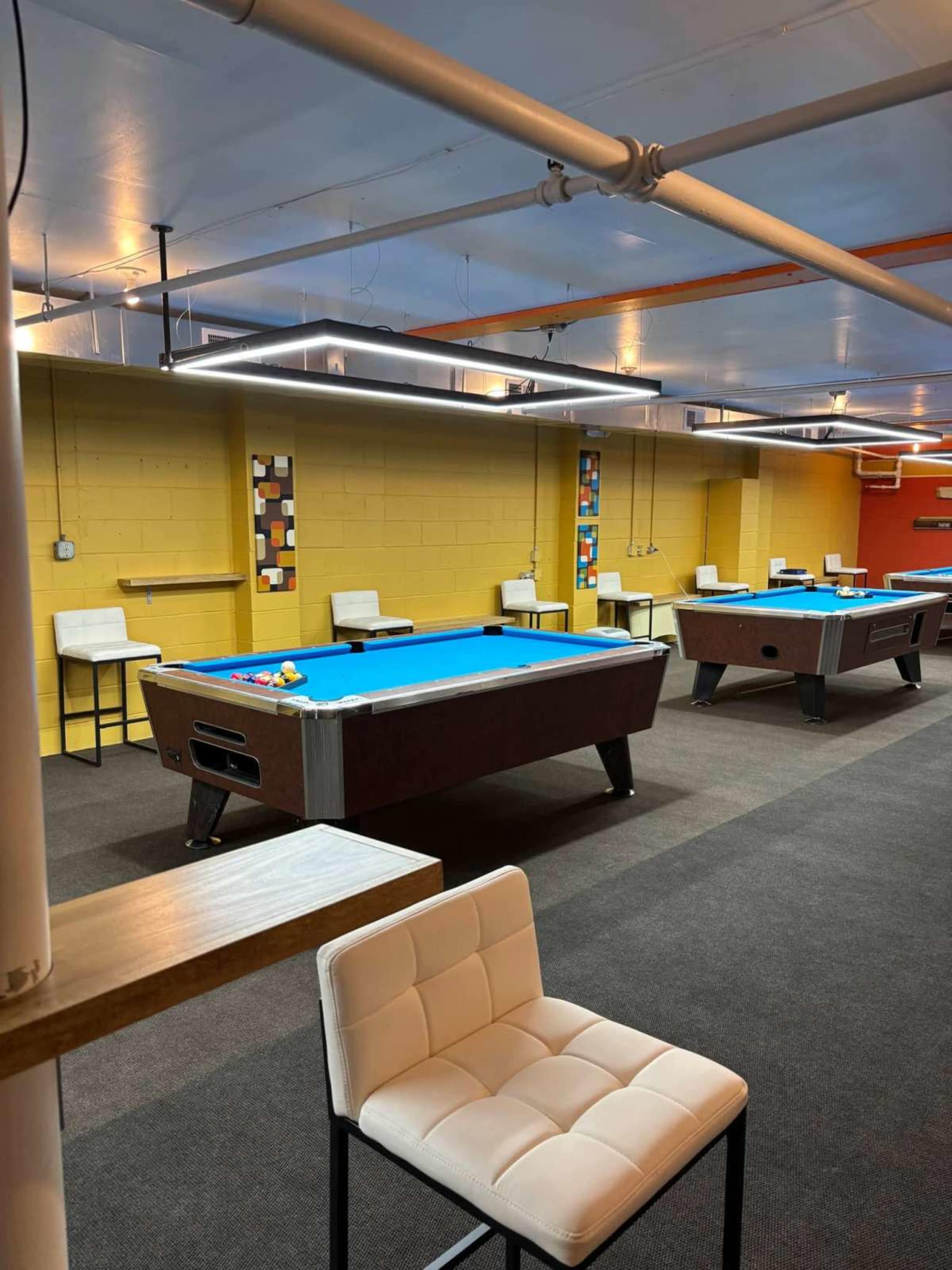 The image shows a spacious billiard room with several pool tables and modern lighting fixtures.