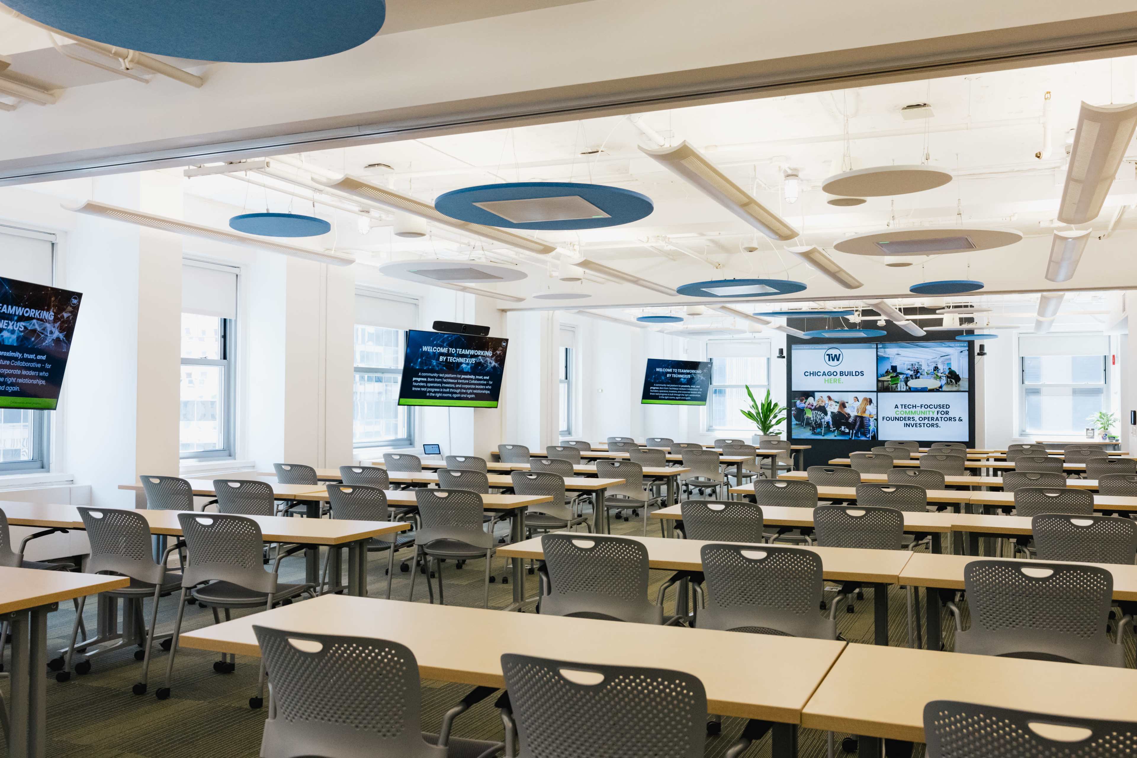A modern classroom features rows of tables and chairs surrounded by large screens displaying information on the walls.