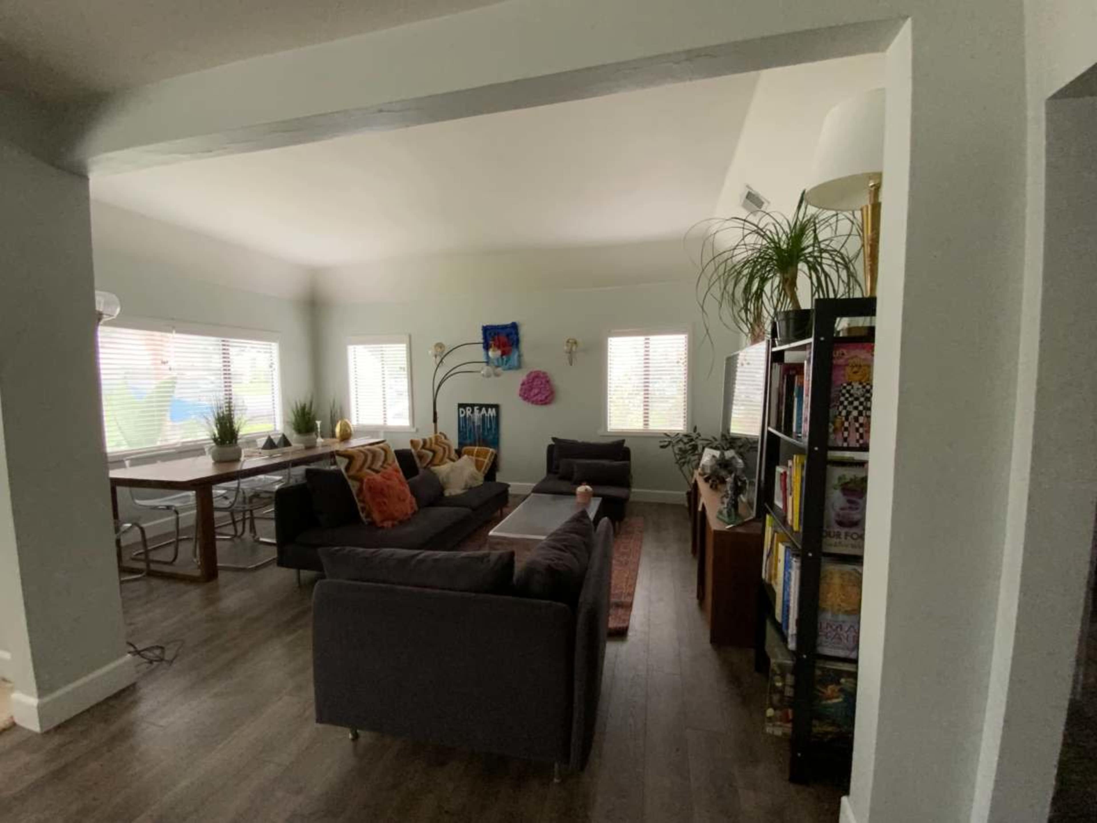 The image shows a living room with two dark sofas, a coffee table, and a dining area with a large table, all under soft lighting.