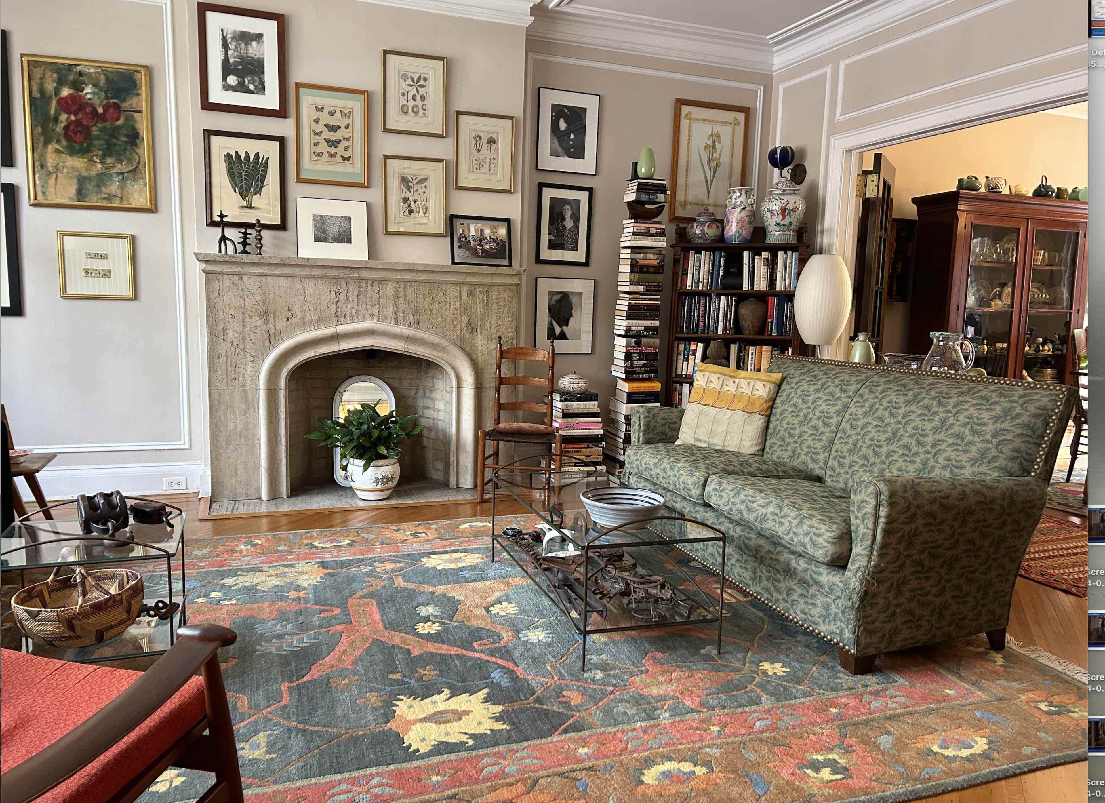 A living room features a green patterned sofa, a stone fireplace, a large area rug, and walls adorned with framed artwork.
