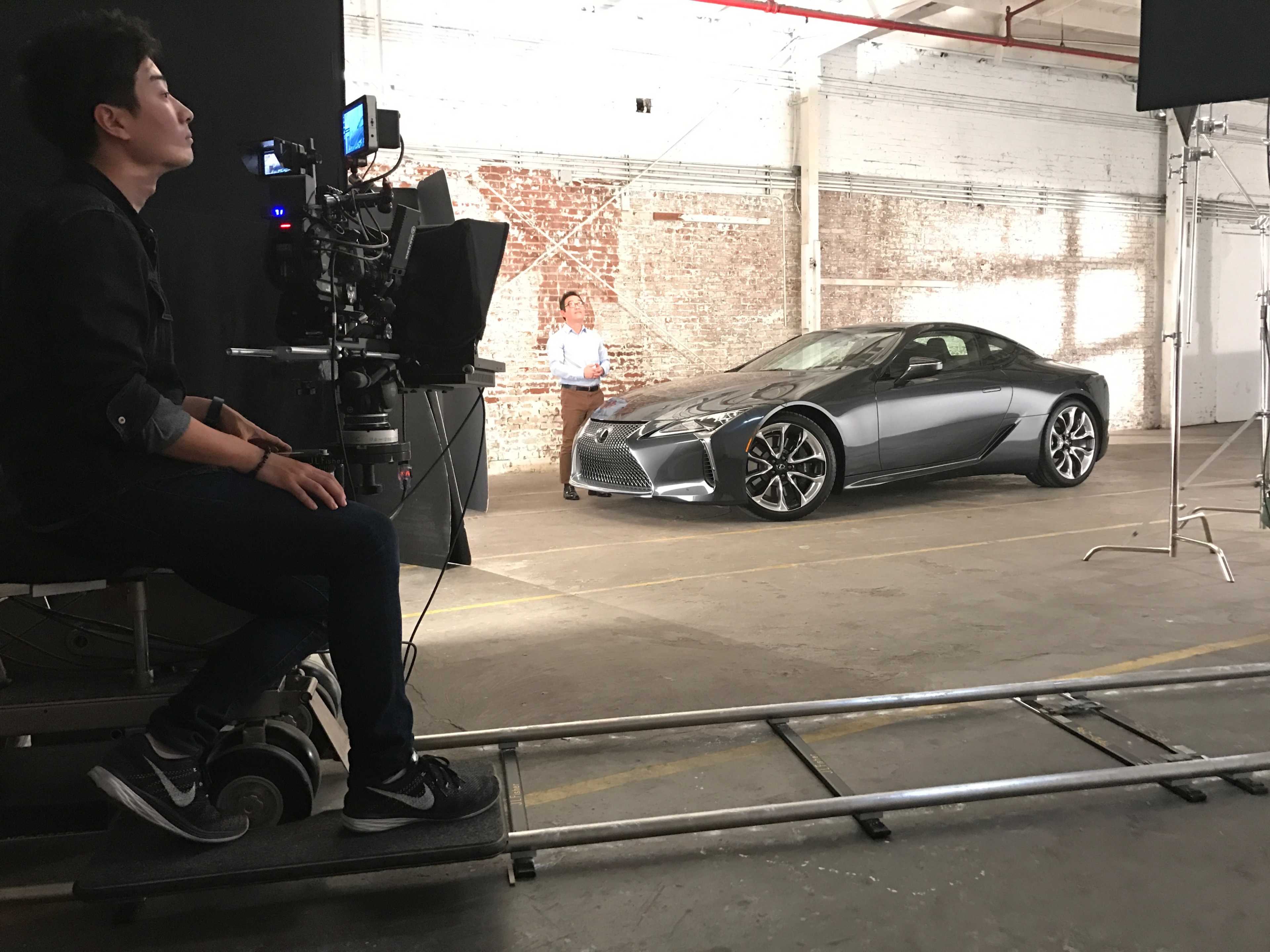 A film crew sets up a shot featuring a sleek car in an industrial space with brick walls.
