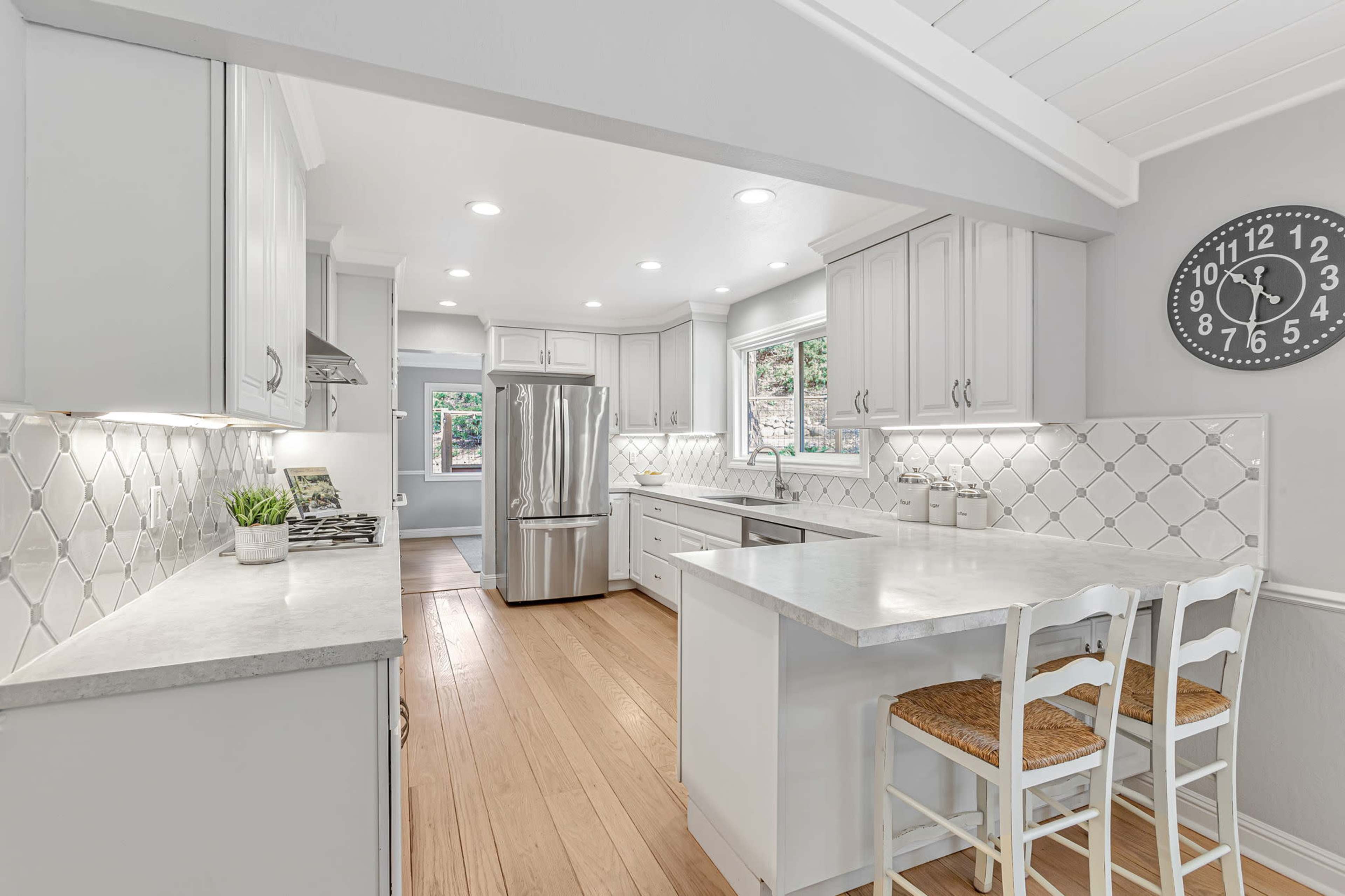 The kitchen features white cabinetry, stainless steel appliances, and a large island with two seating chairs.