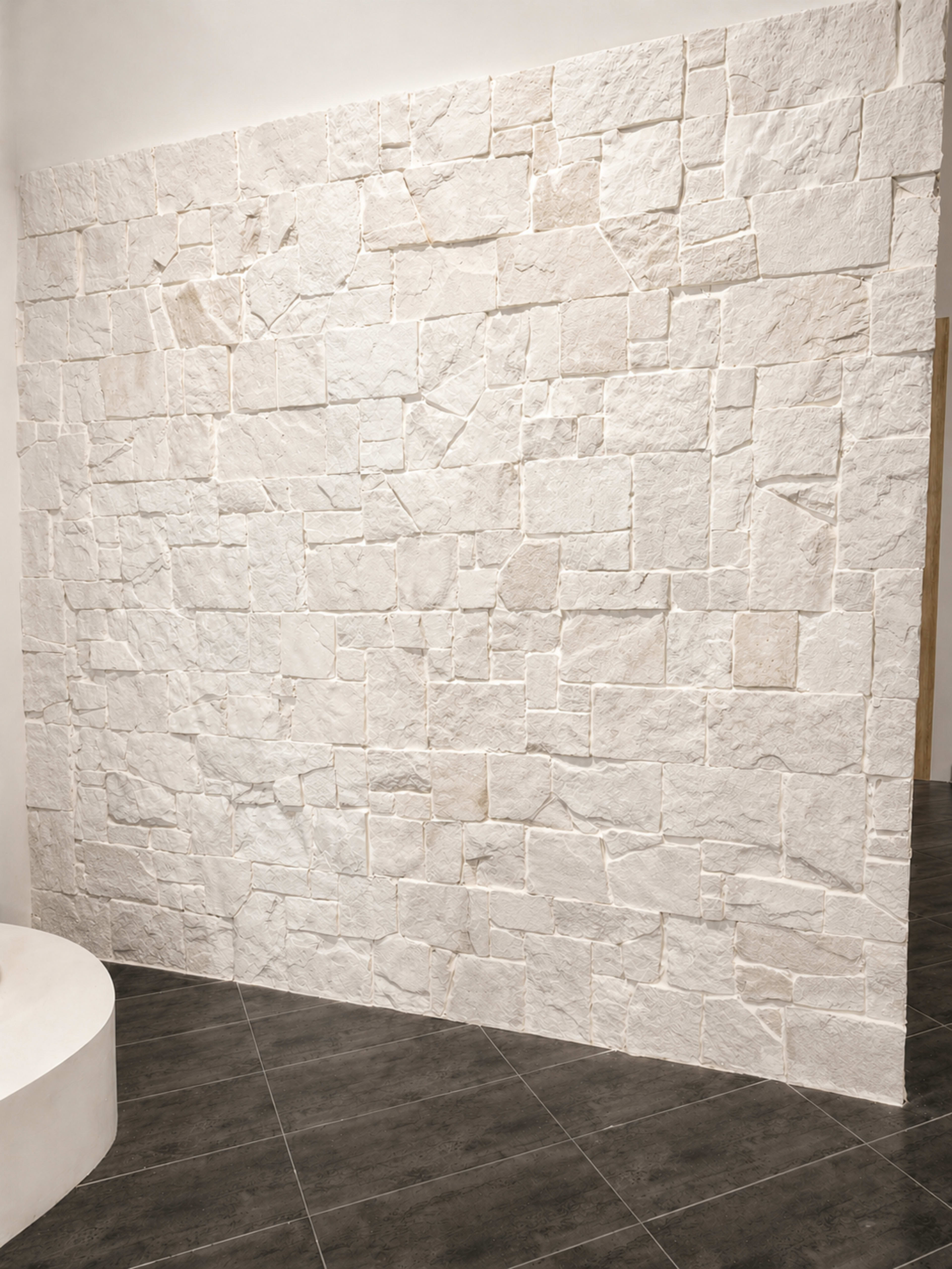 The image shows a textured white stone wall next to a circular base and dark tiled flooring.
