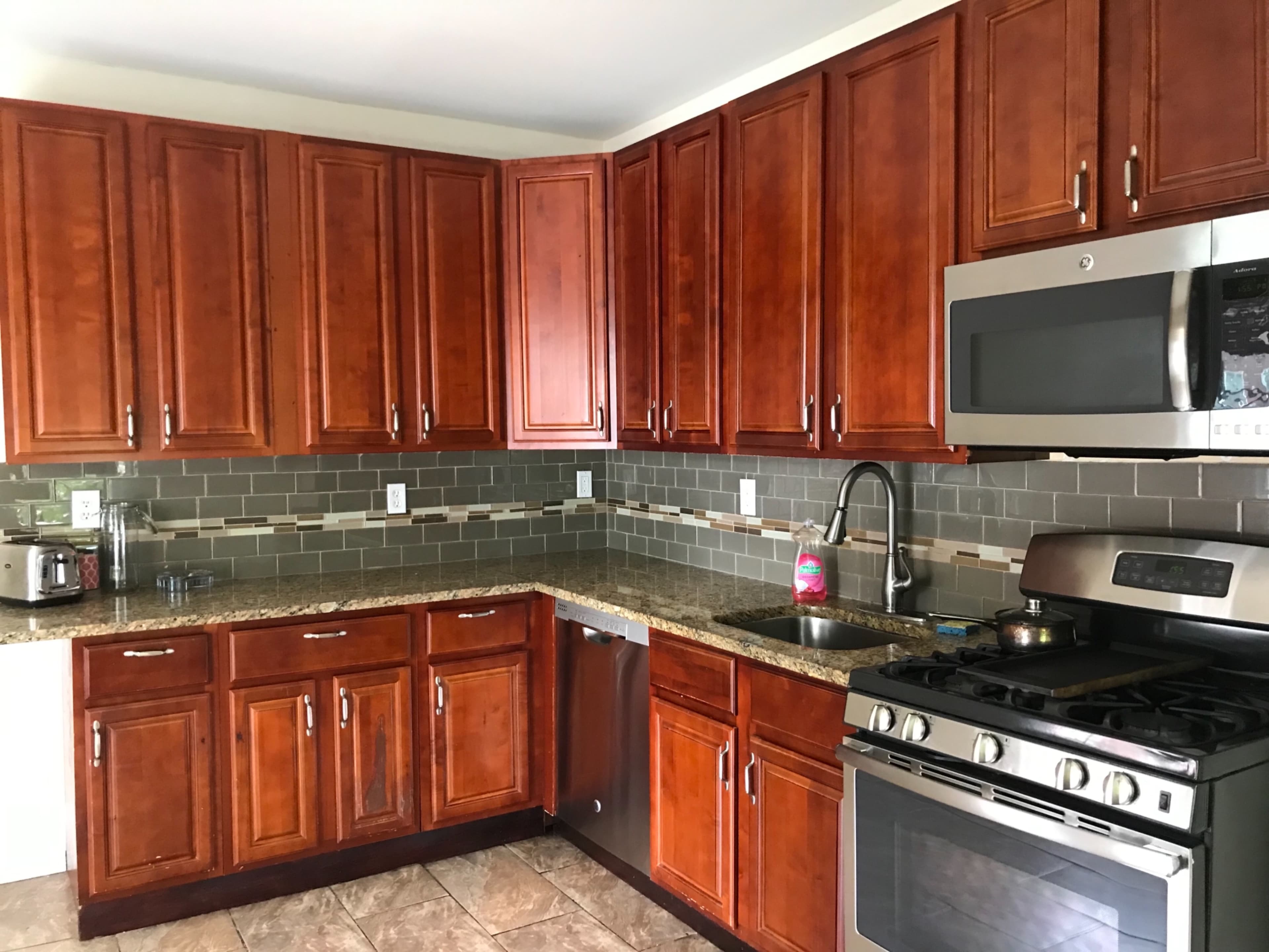 The image shows a kitchen with wooden cabinetry, stainless steel appliances, and a granite countertop.