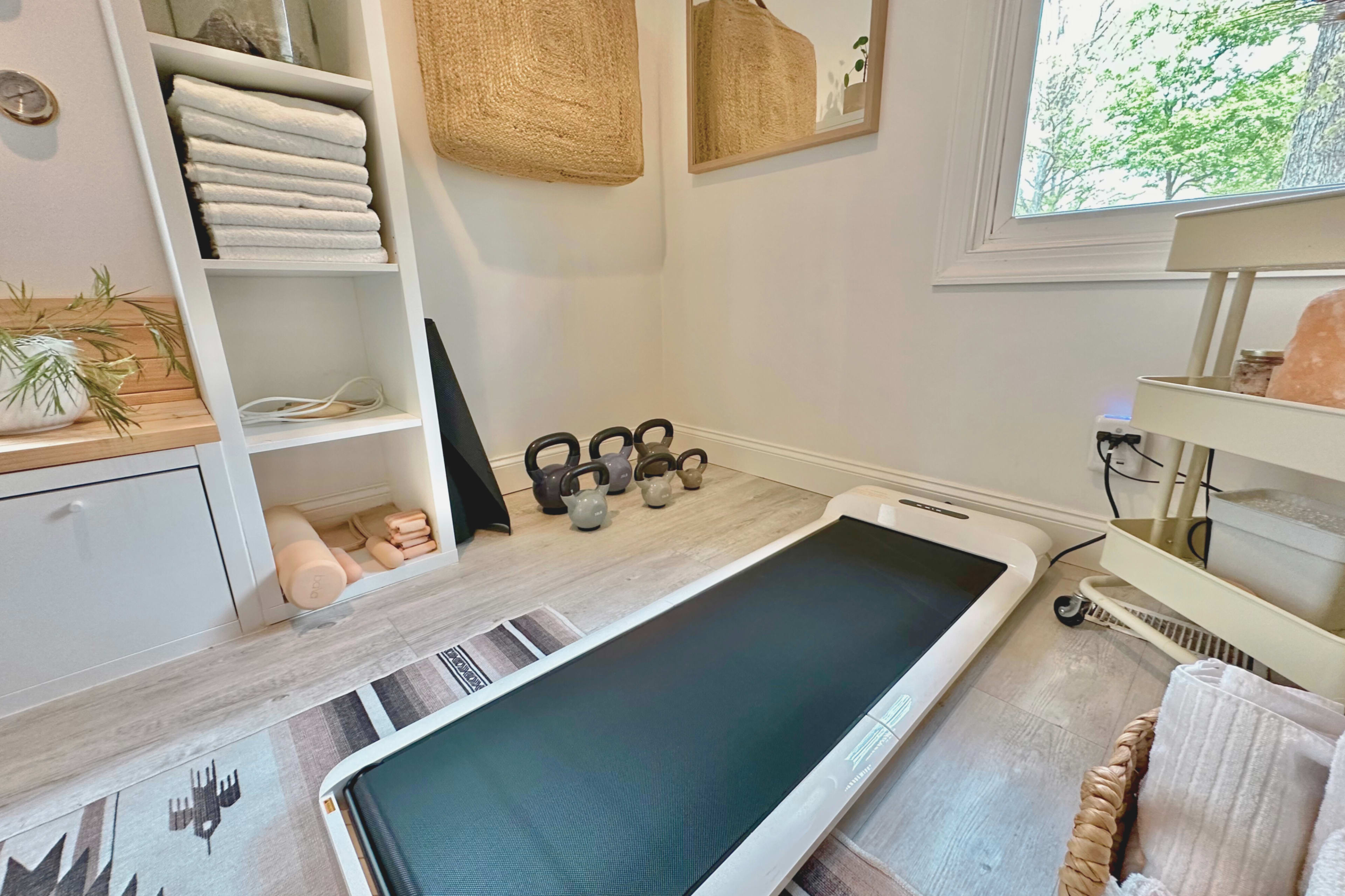 A minimalistic fitness space featuring a treadmill, kettlebells, towels, and storage shelves.
